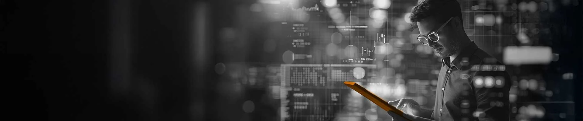 A man wearing glasses is looking at a tablet in a dark room with digital financial charts and graphs overlayed in the background.
