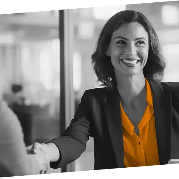 A woman in business attire smiling and shaking hands in an office setting.