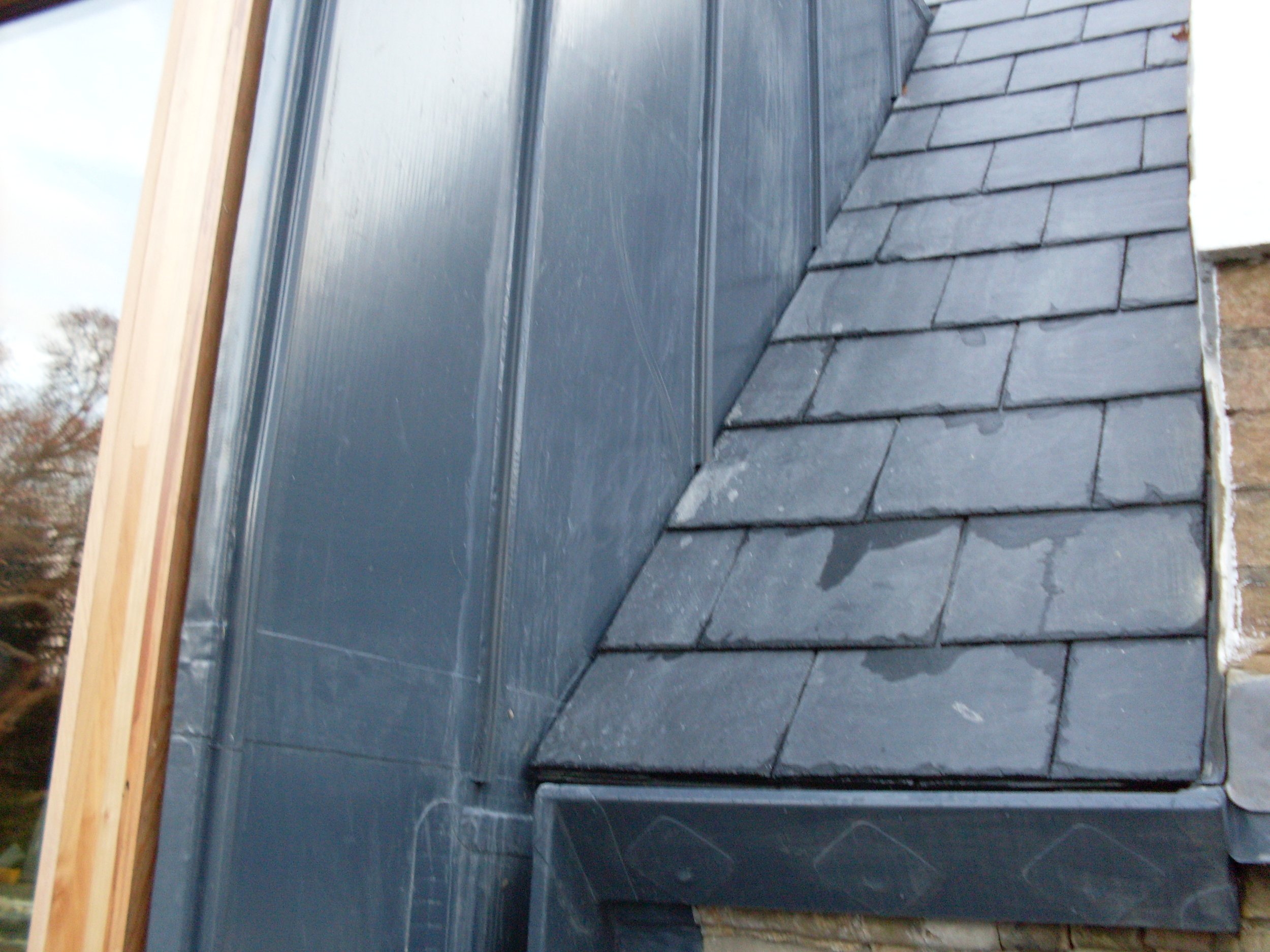 Close-up of a roof with dark gray asphalt shingles and a section of metal flashing along the edge.