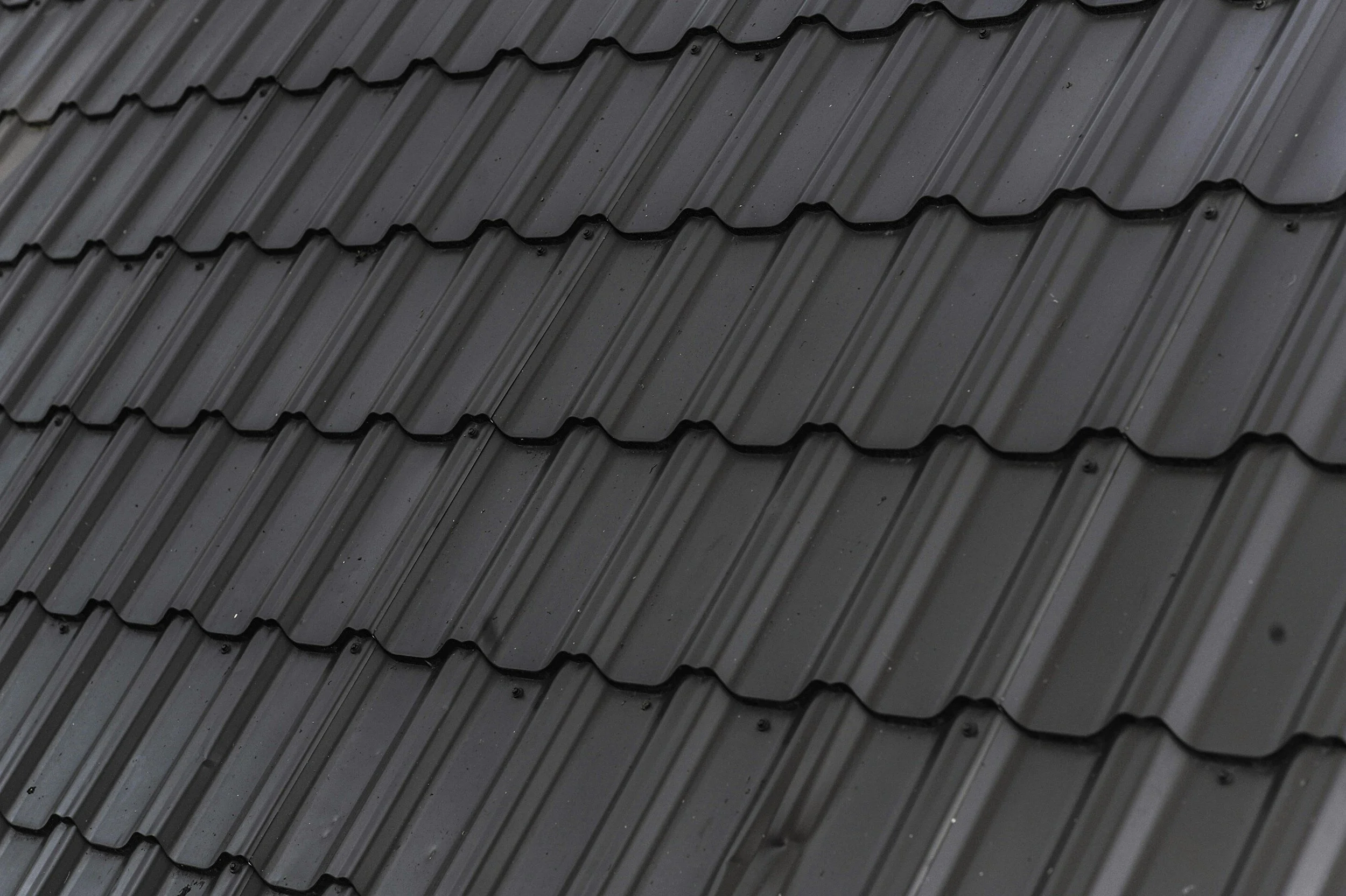 Close-up of black metal roofing shingles arranged in overlapping rows.