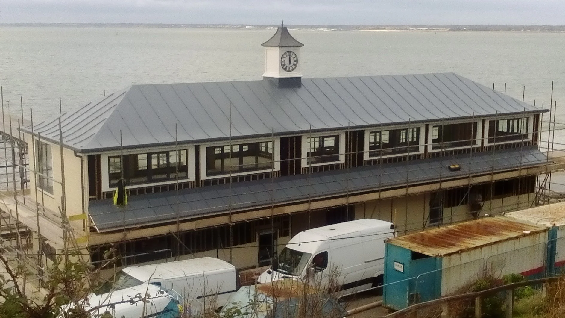 Building under construction near a body of water with a clock tower on the roof.