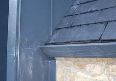 Close-up of a metal and shingled roof edge with a brick wall underneath.