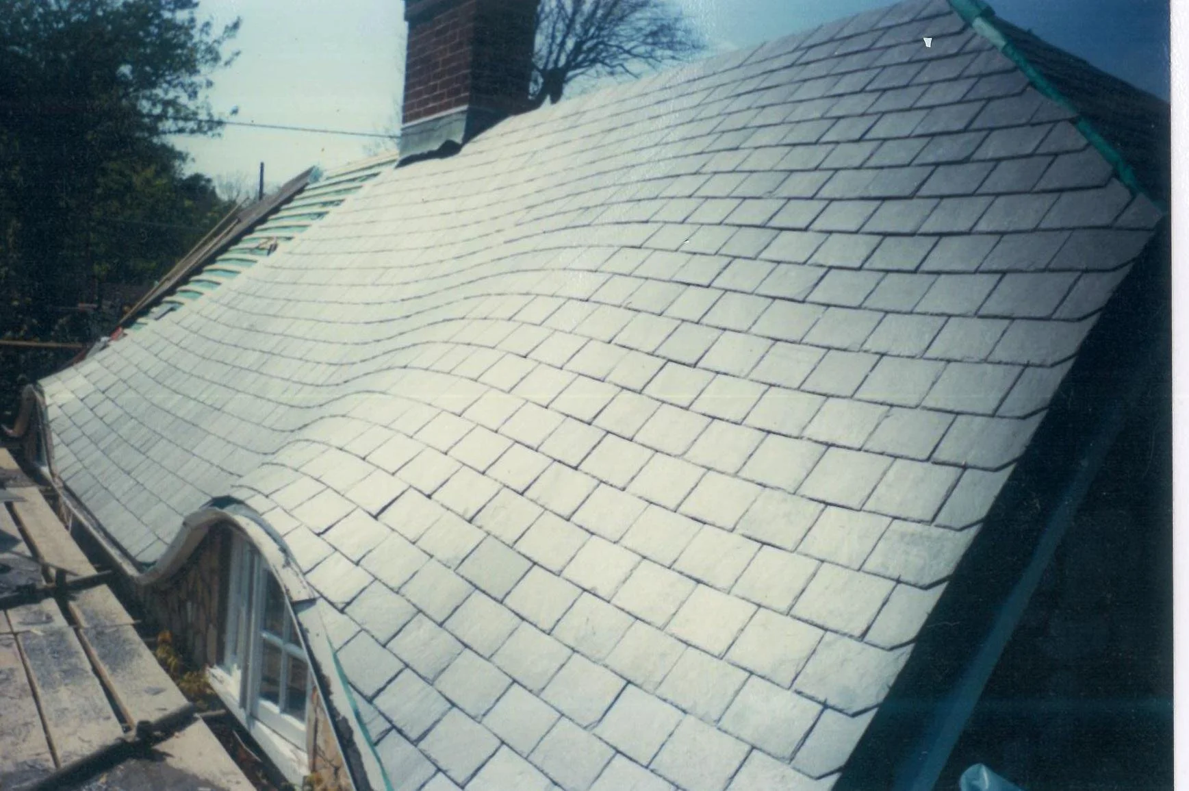 View of a house roof with new light gray shingles, with some construction materials and a ladder visible in the foreground.