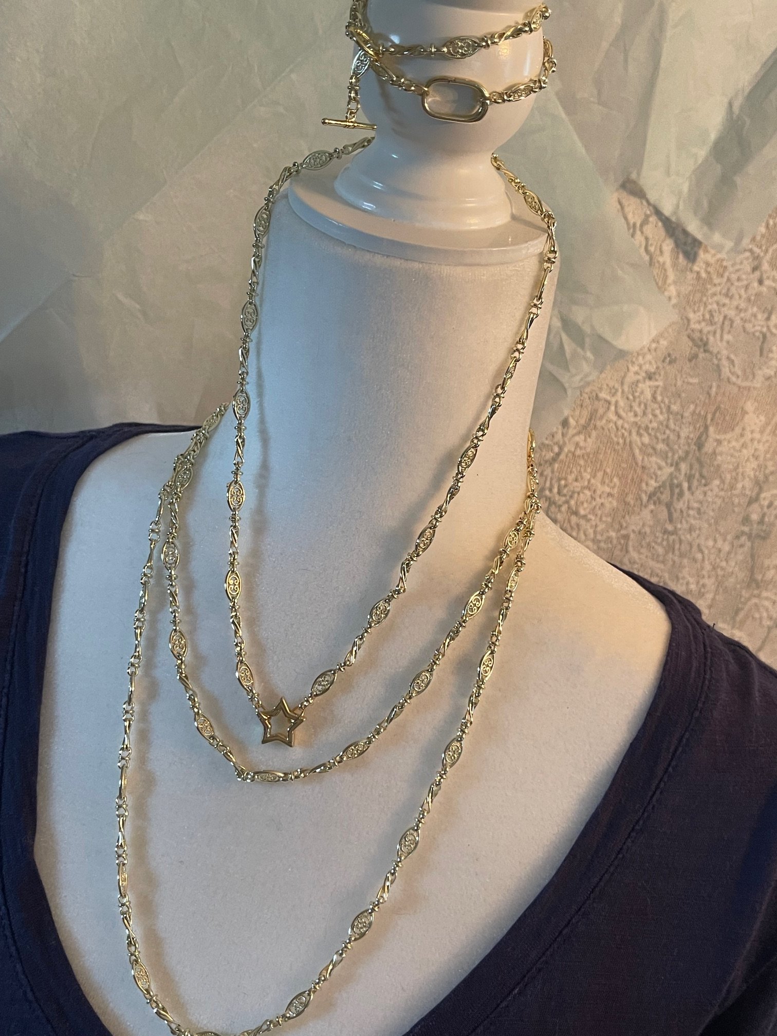 Display of layered gold necklaces with various chain links, a star-shaped pendant, and other decorative charms.