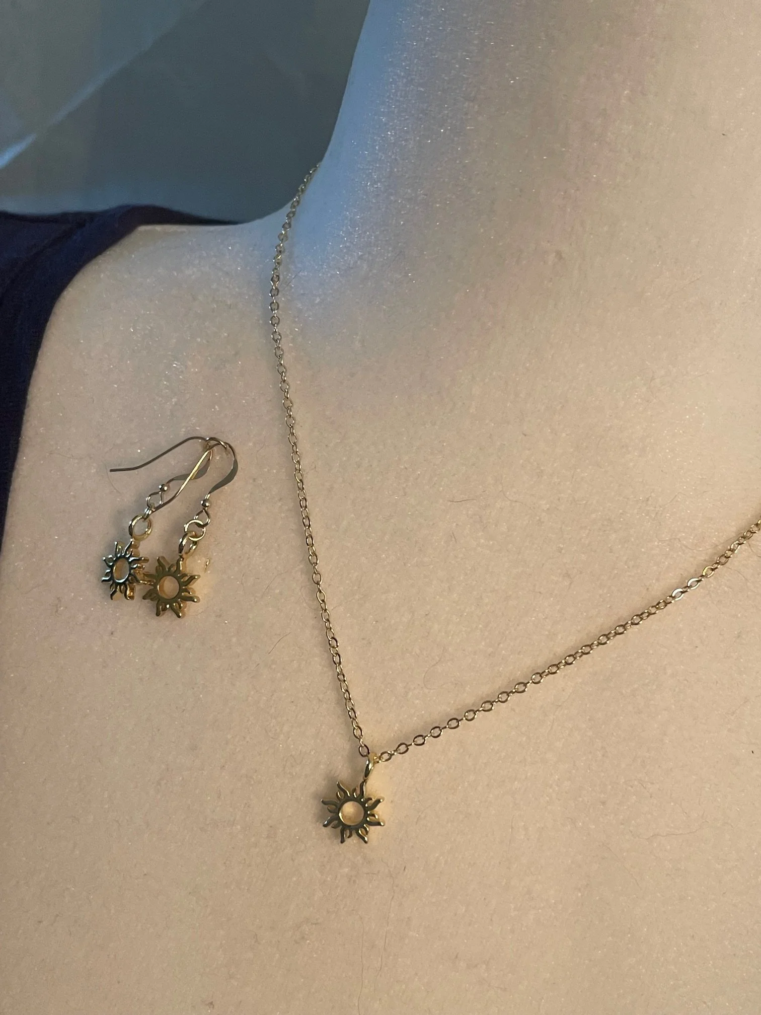 Gold sun-shaped jewelry set with necklace and earrings displayed on a person's neck and shoulder.