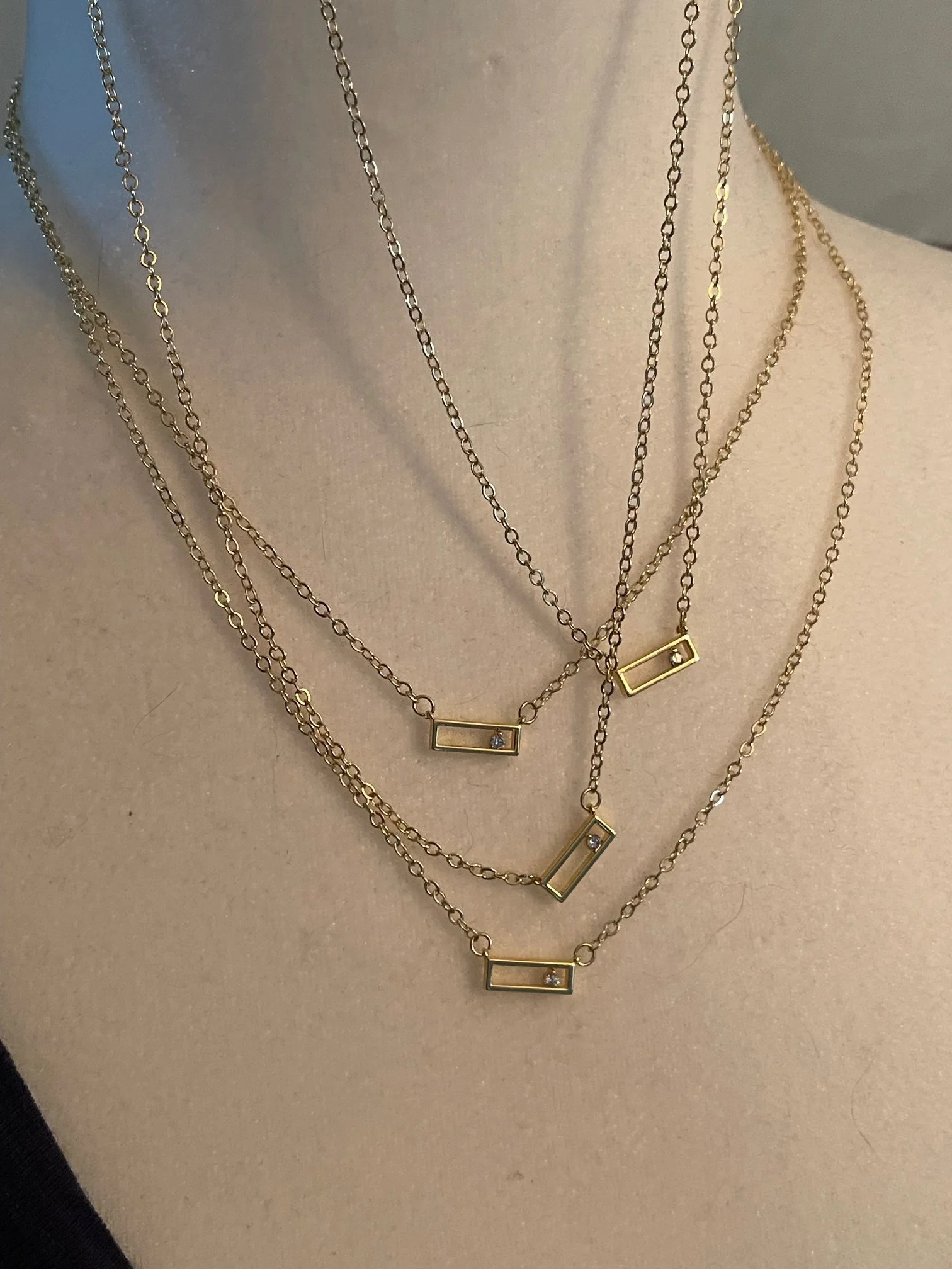 Four layered gold necklaces with rectangular pendants and small cubic zirconia displayed on a mannequin.
