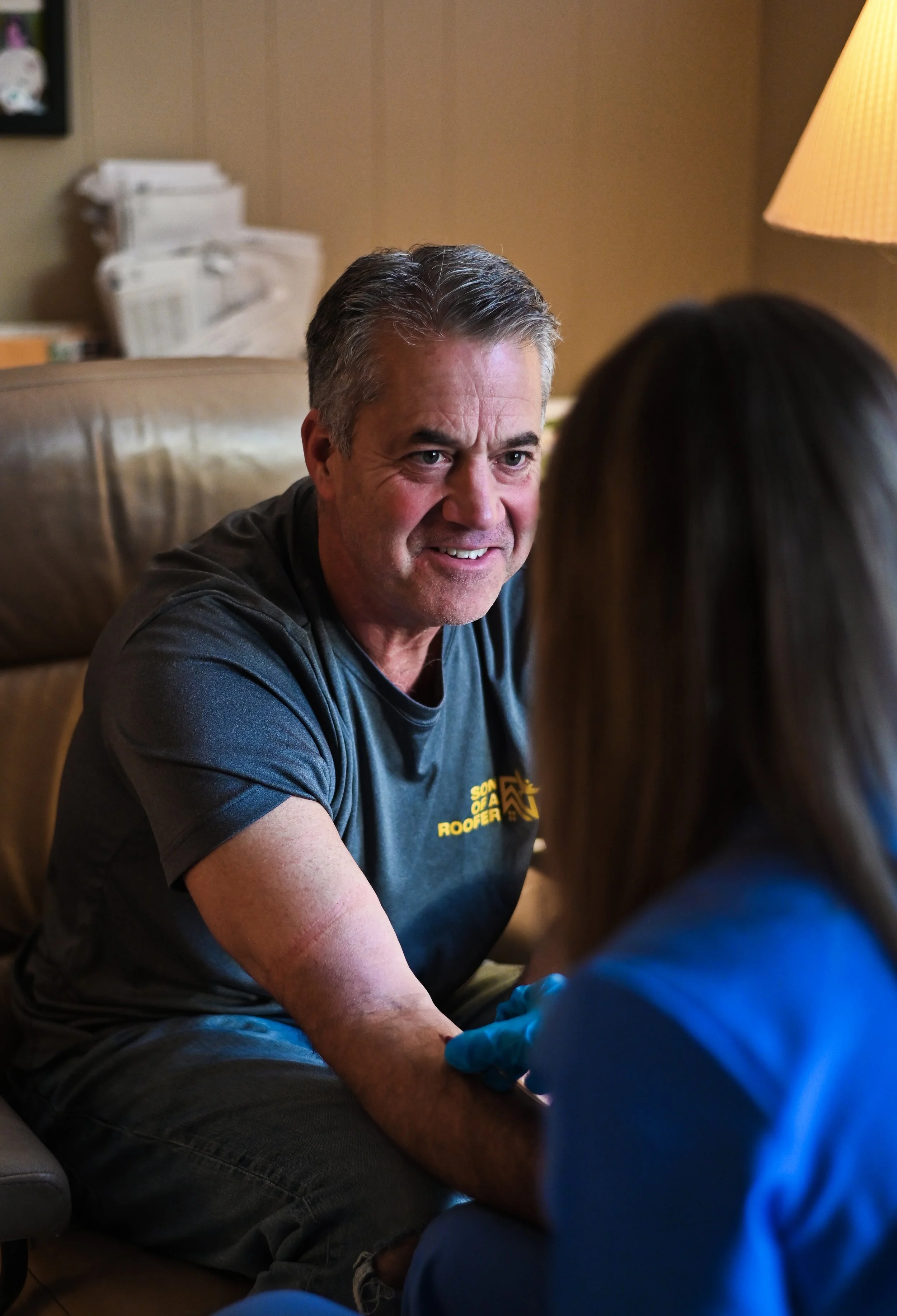 A man receiving a peripheral IV from a licensed healthcare professional in a home setting.