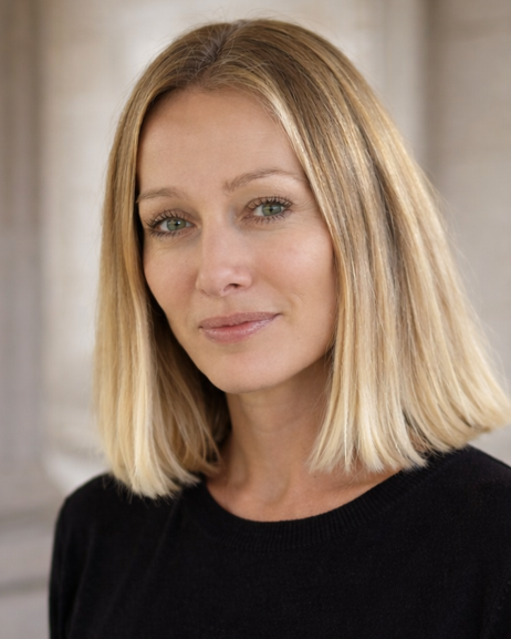 Une femme aux cheveux blonds portant un haut noir, regardant vers l'objectif