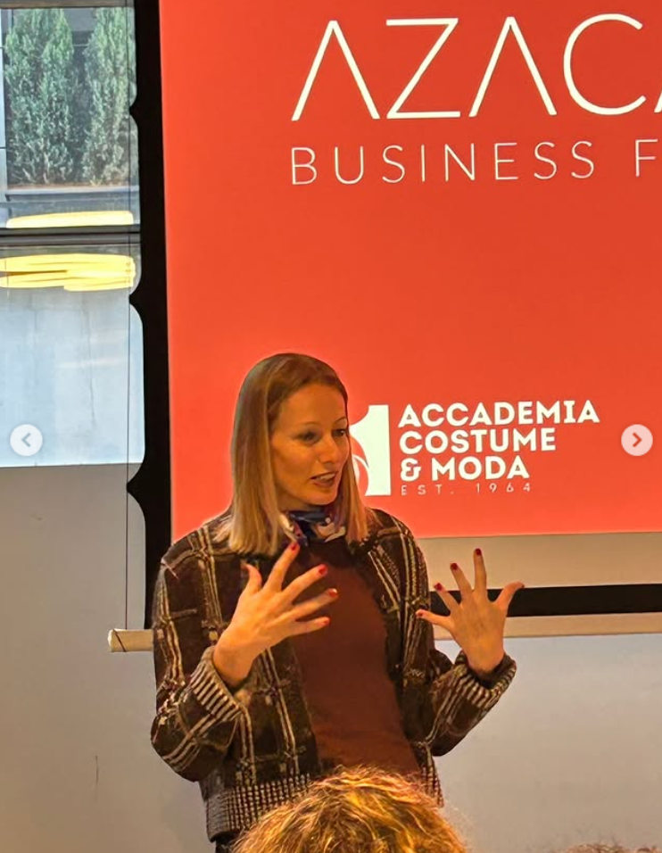 Une femme parle lors d'une présentation ou conférence, avec un arrière-plan orange affichant le logo AZAC, et des textes mentionnant une académie de costume et mode