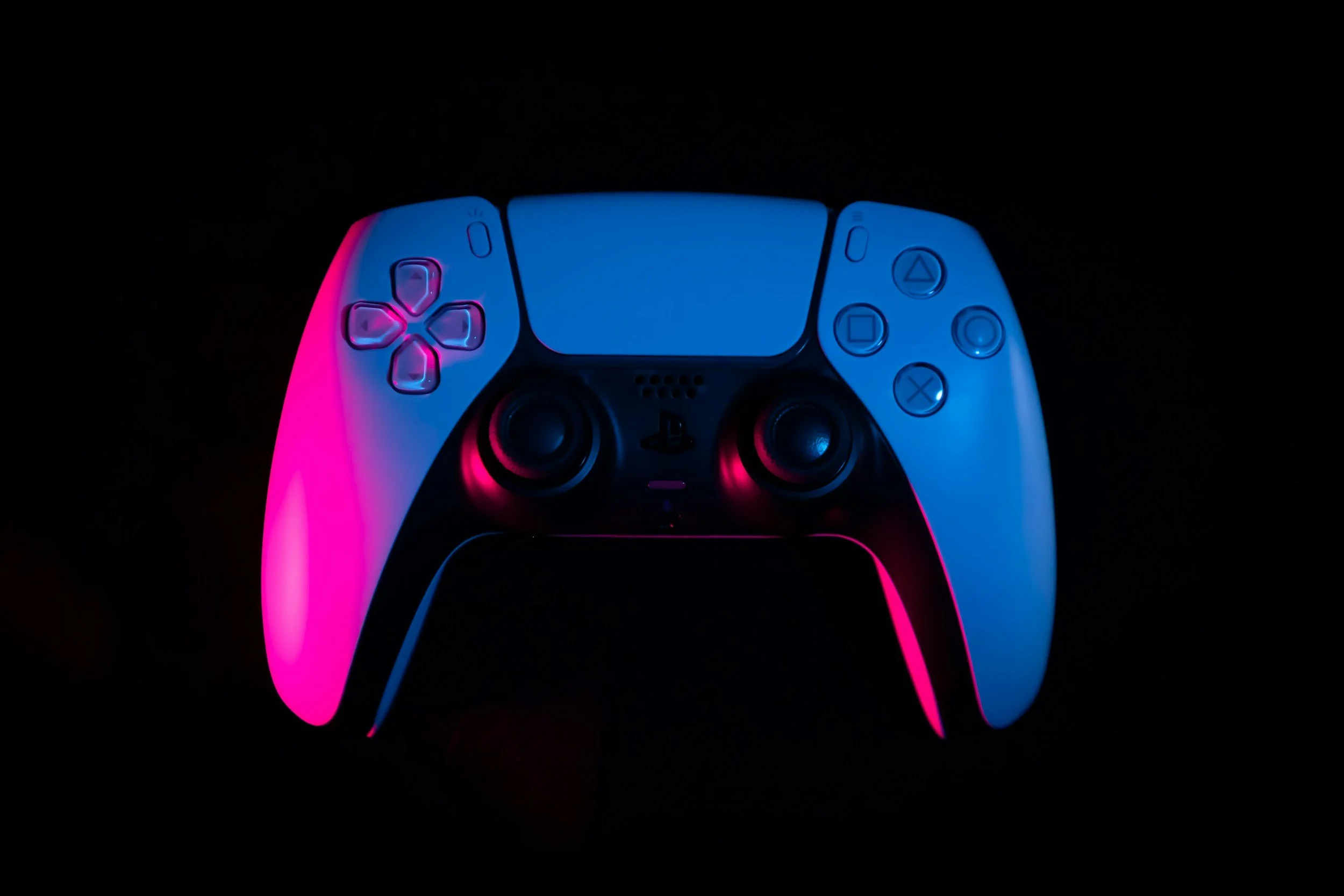 A modern gaming controller illuminated with blue and pink lights against a black background.