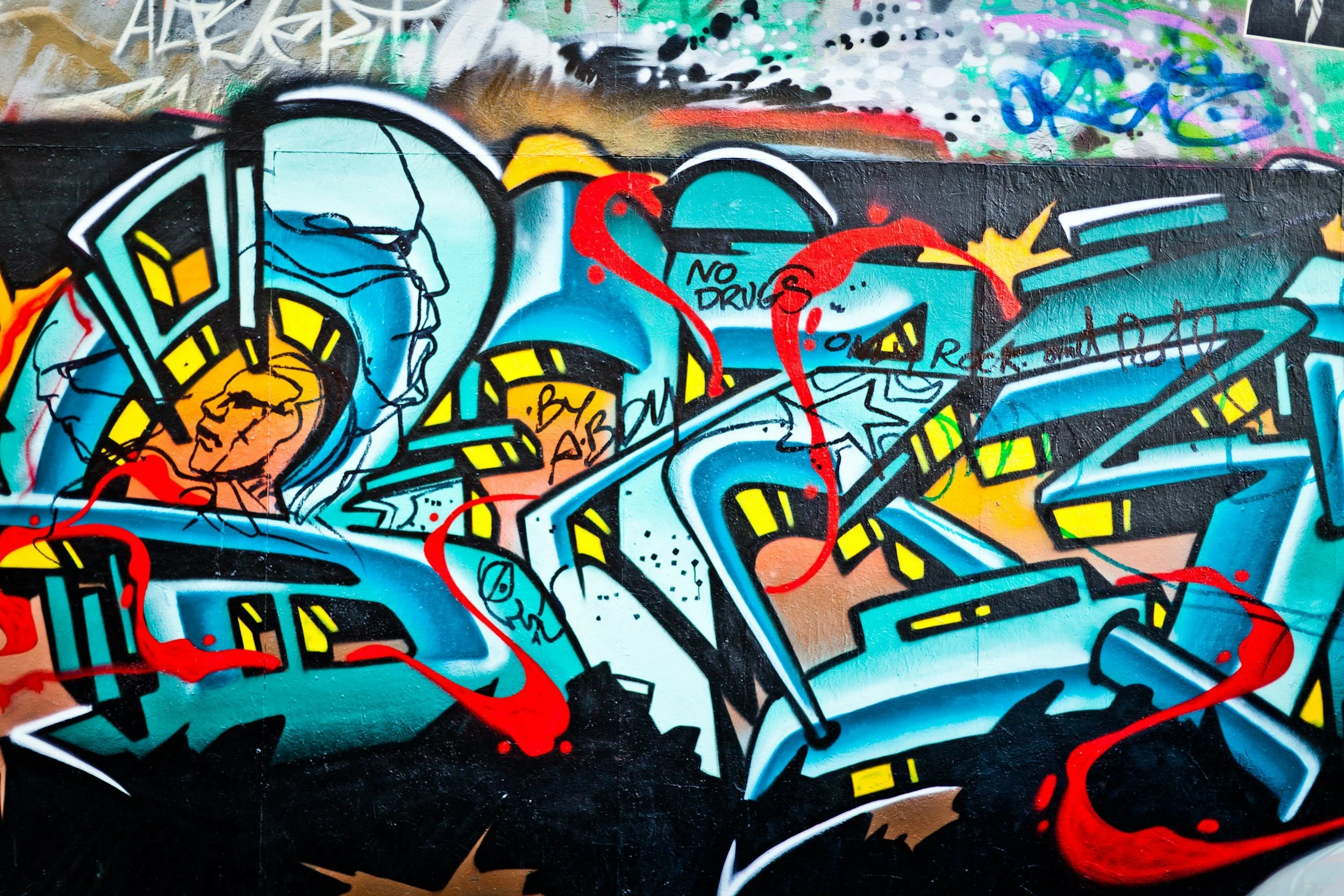 Colorful graffiti on a wall featuring a detailed illustration of a person's face in profile, vibrant abstract shapes, and street-style lettering.