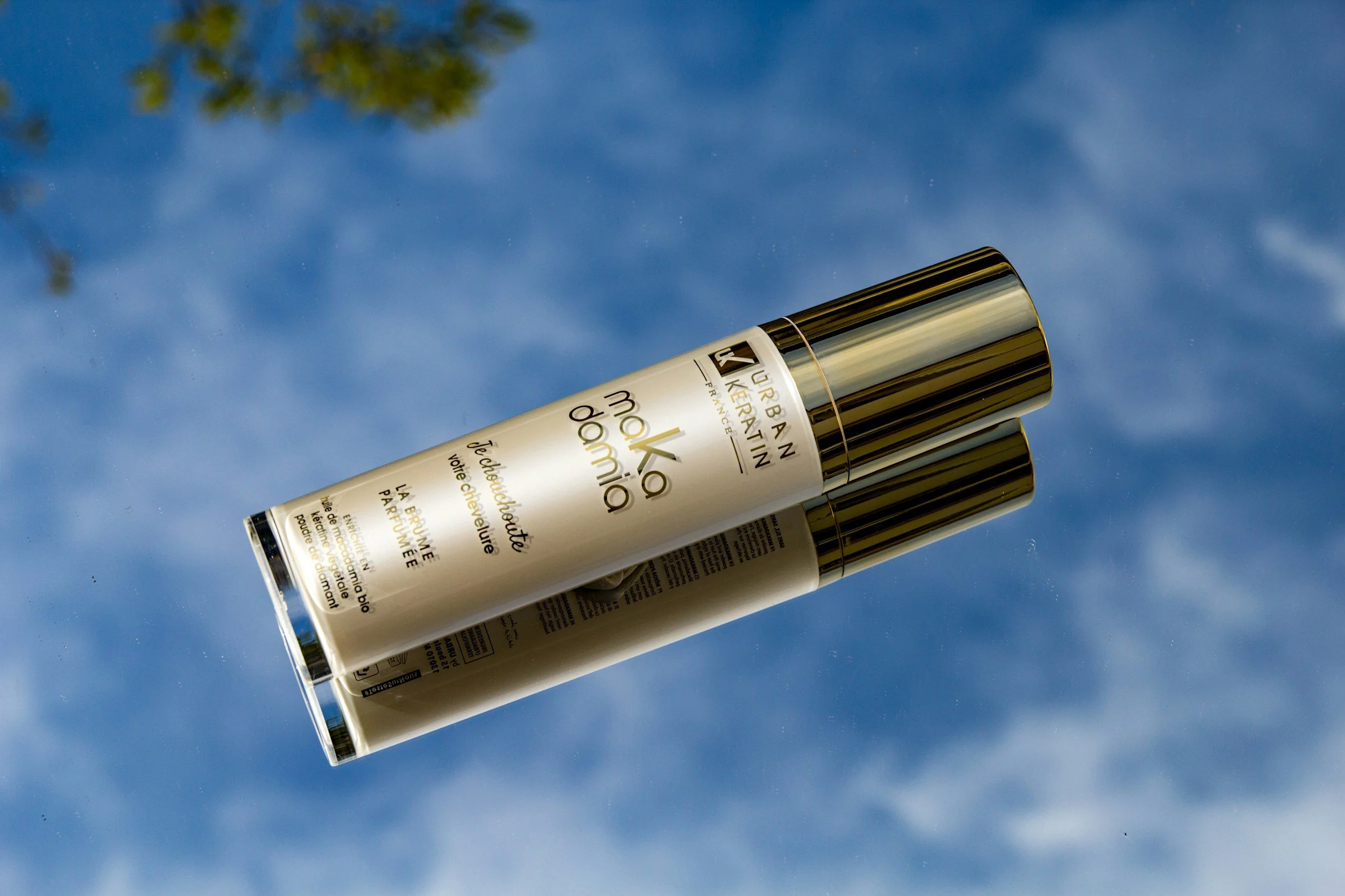 Two cans of Urban Keratin moisturizer for blond hair, lying on a reflective surface with a sky and clouds background.