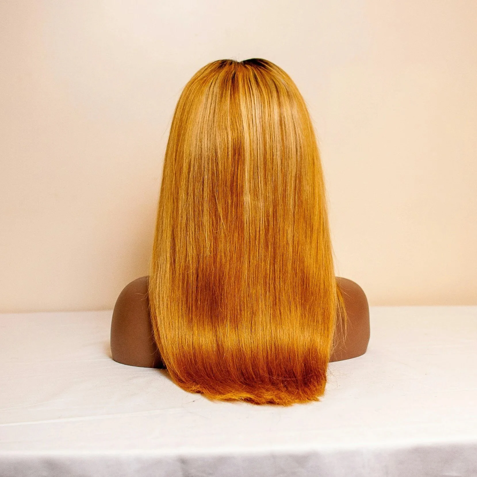 Back view of a mannequin with long, straight, blonde hair on a white surface against a plain wall.