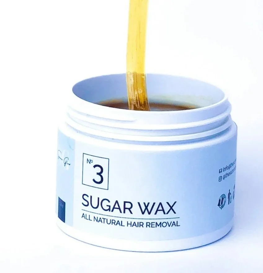 A jar of sugar wax with a spatula dipping into it, labeled for all natural hair removal.