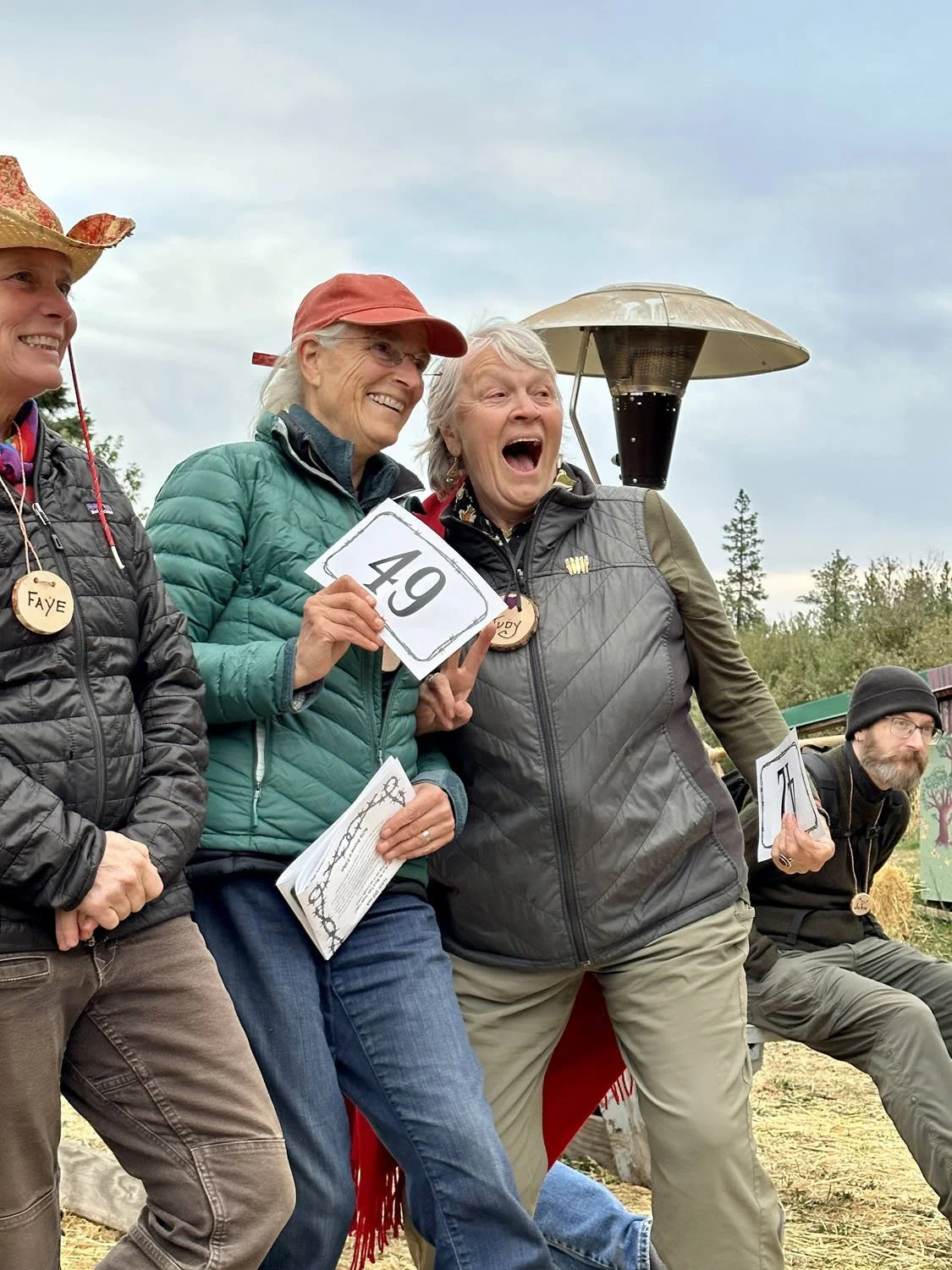Group of people outdoors, celebrating and holding numbered signs, with smiles and excitement, one person appears to be laughing, and others are dressed in outdoor clothing.