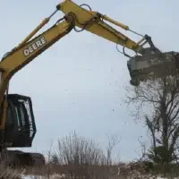 A medium sized tree is shredded from the top down by the extended mechanical arm and mulching heads of a John Deere 250G Excavators with FAE Mulching Heads