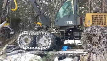 A close up image of a forest harvester partially covered in snow crossing a temporary bridge with thick forest in the background.