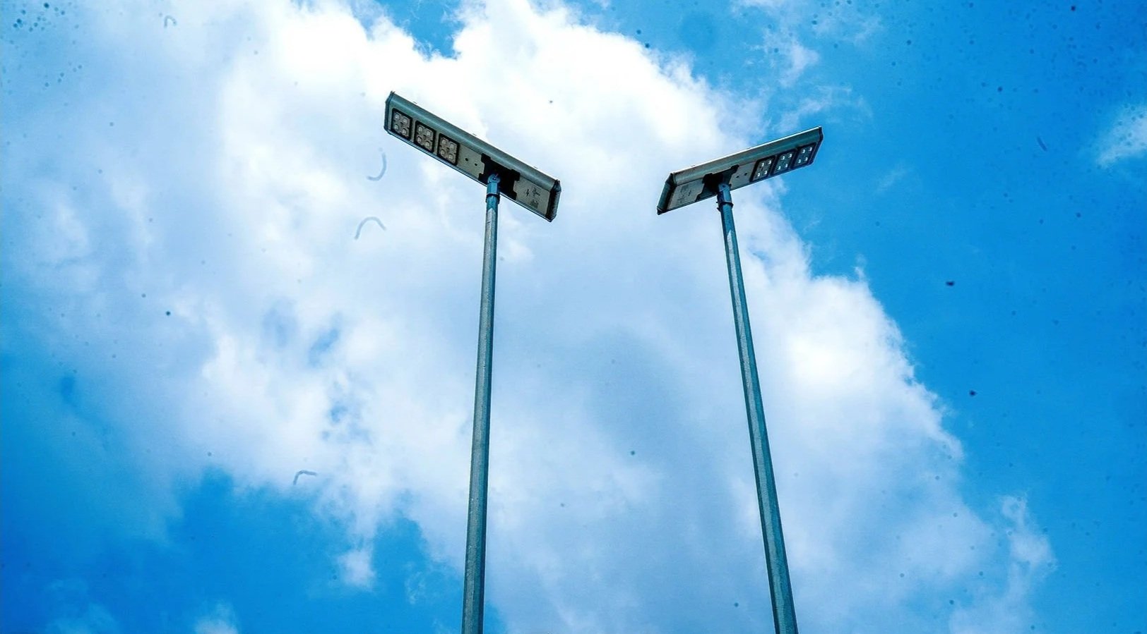Two streetlights with solar panels on top against a partly cloudy blue sky.