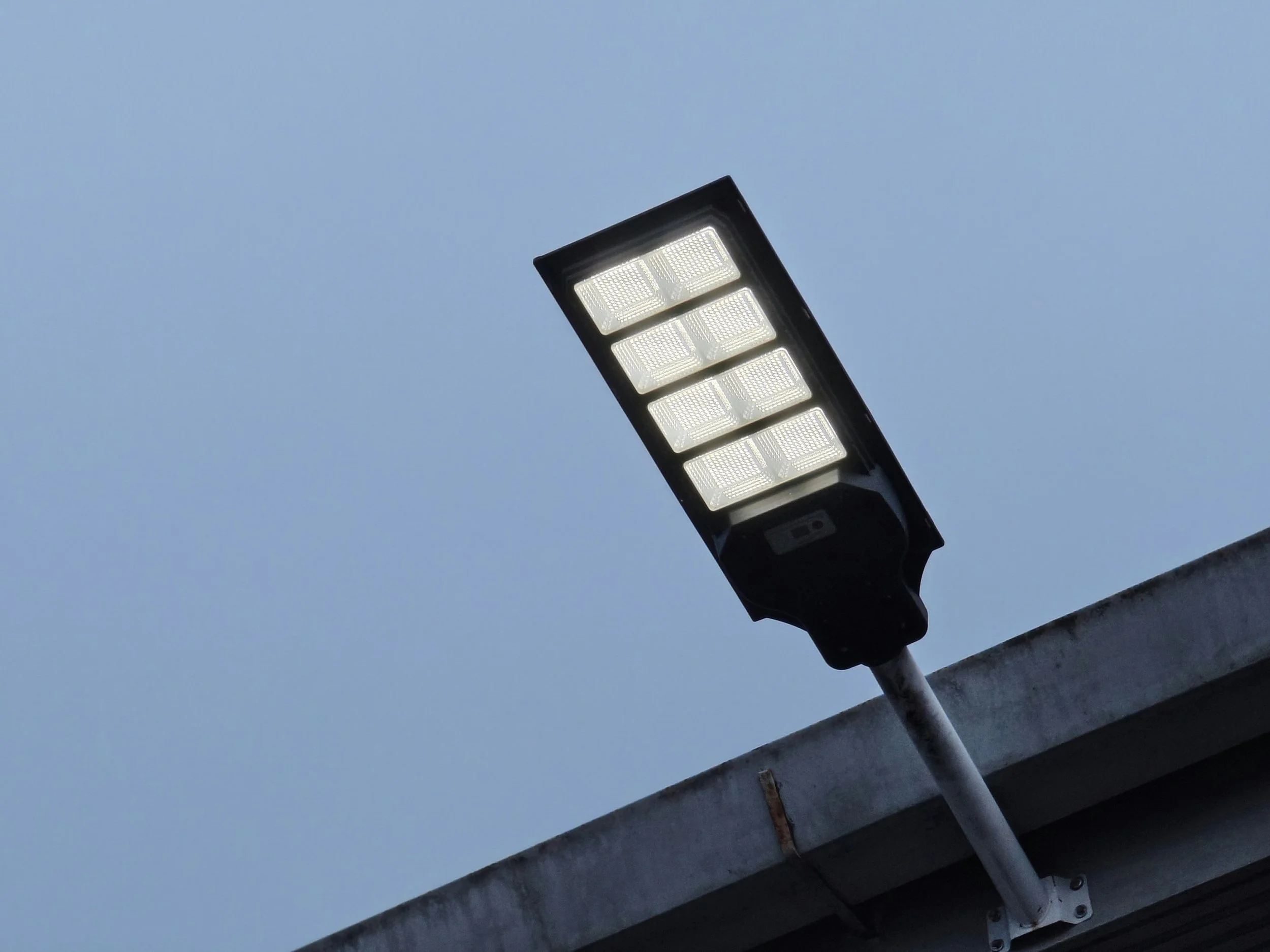 A street light mounted on a pole over a building's edge against a clear sky.