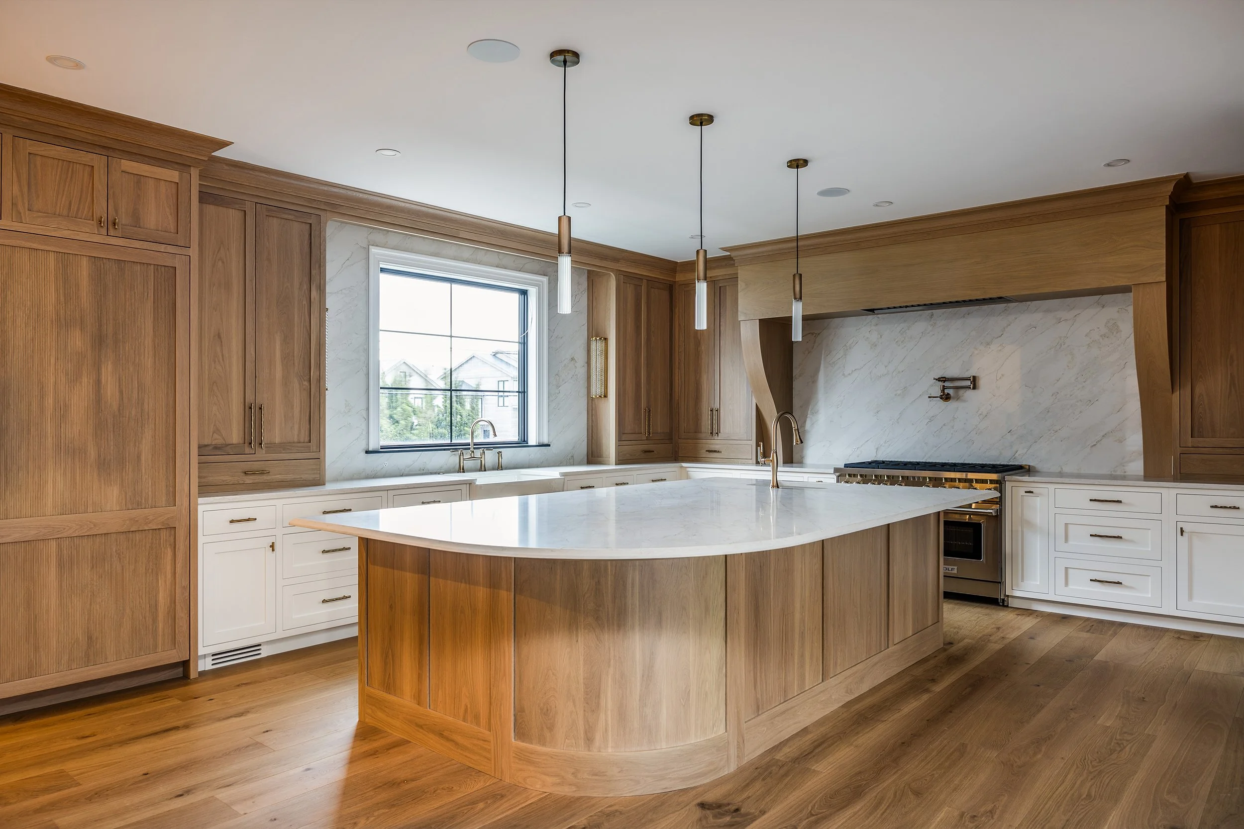 Modern kitchen with wooden cabinets, a large island with white marble countertop, white and wood cabinetry, a window above the sink, and a stove on the right side.