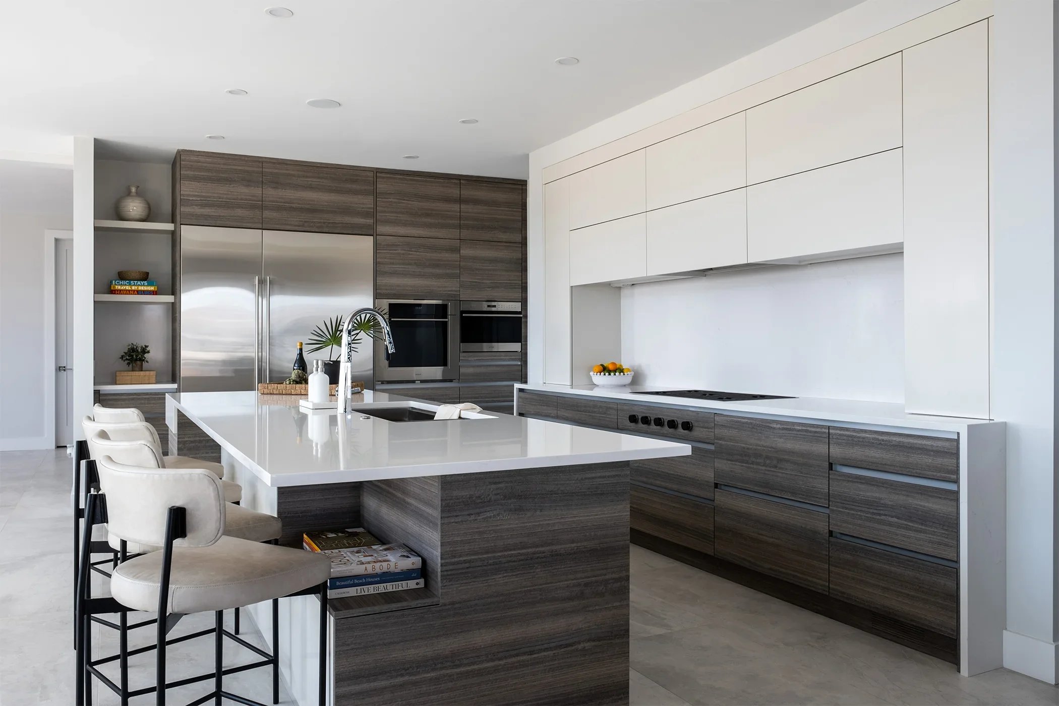 Modern kitchen with white island, beige bar stools, dark wood cabinets, stainless steel appliances, and white upper cabinets.
