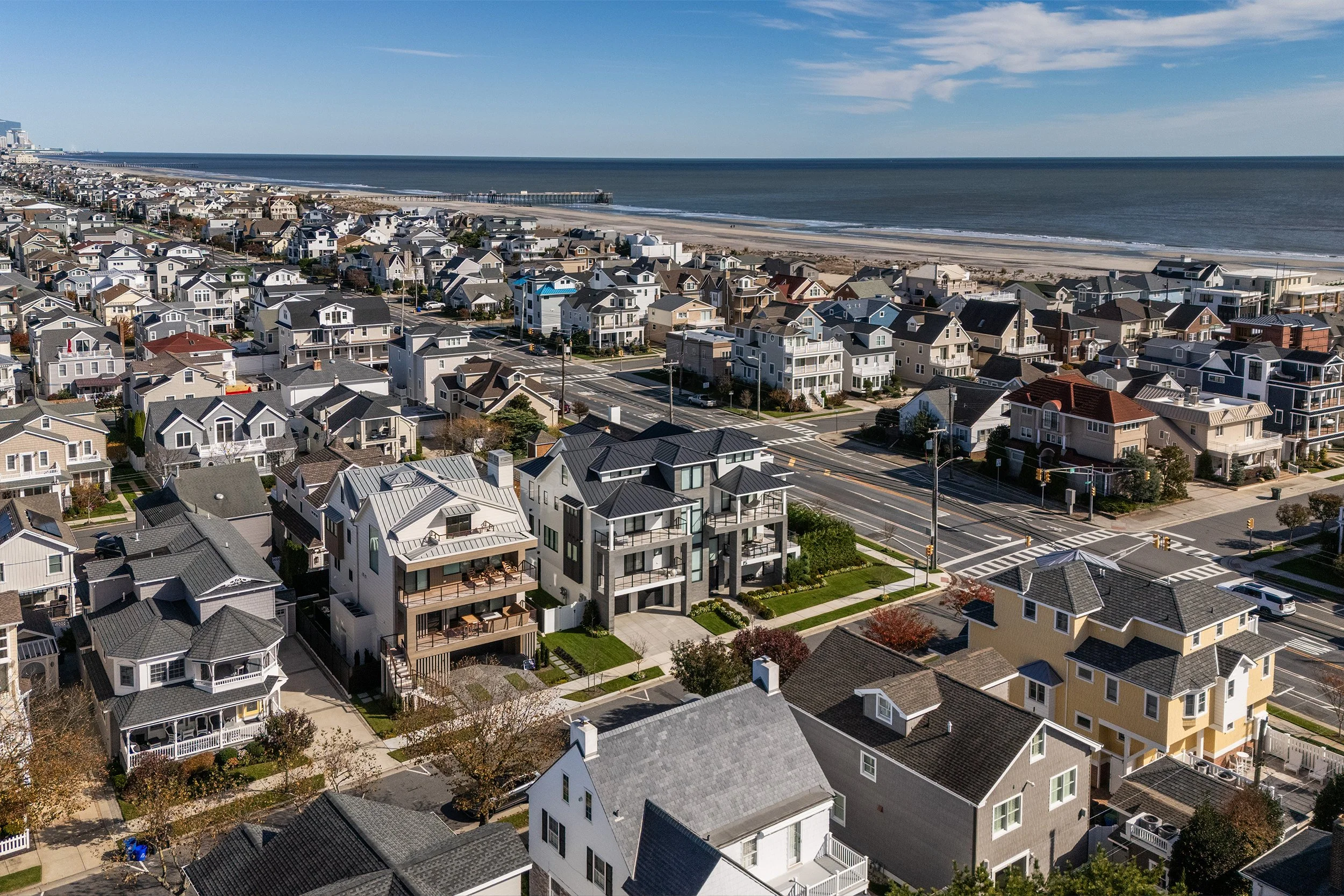 Aerial view of a beachfront residential neighborhood with houses and apartments near the ocean and a pier in the background.