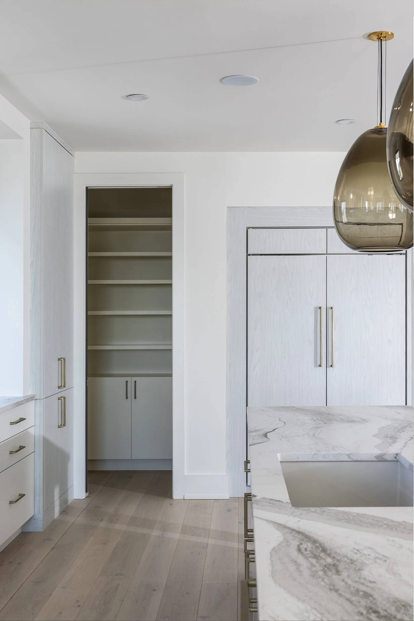 Modern kitchen with white cabinets, marble countertops, and a pantry with open shelves and closed cabinets.