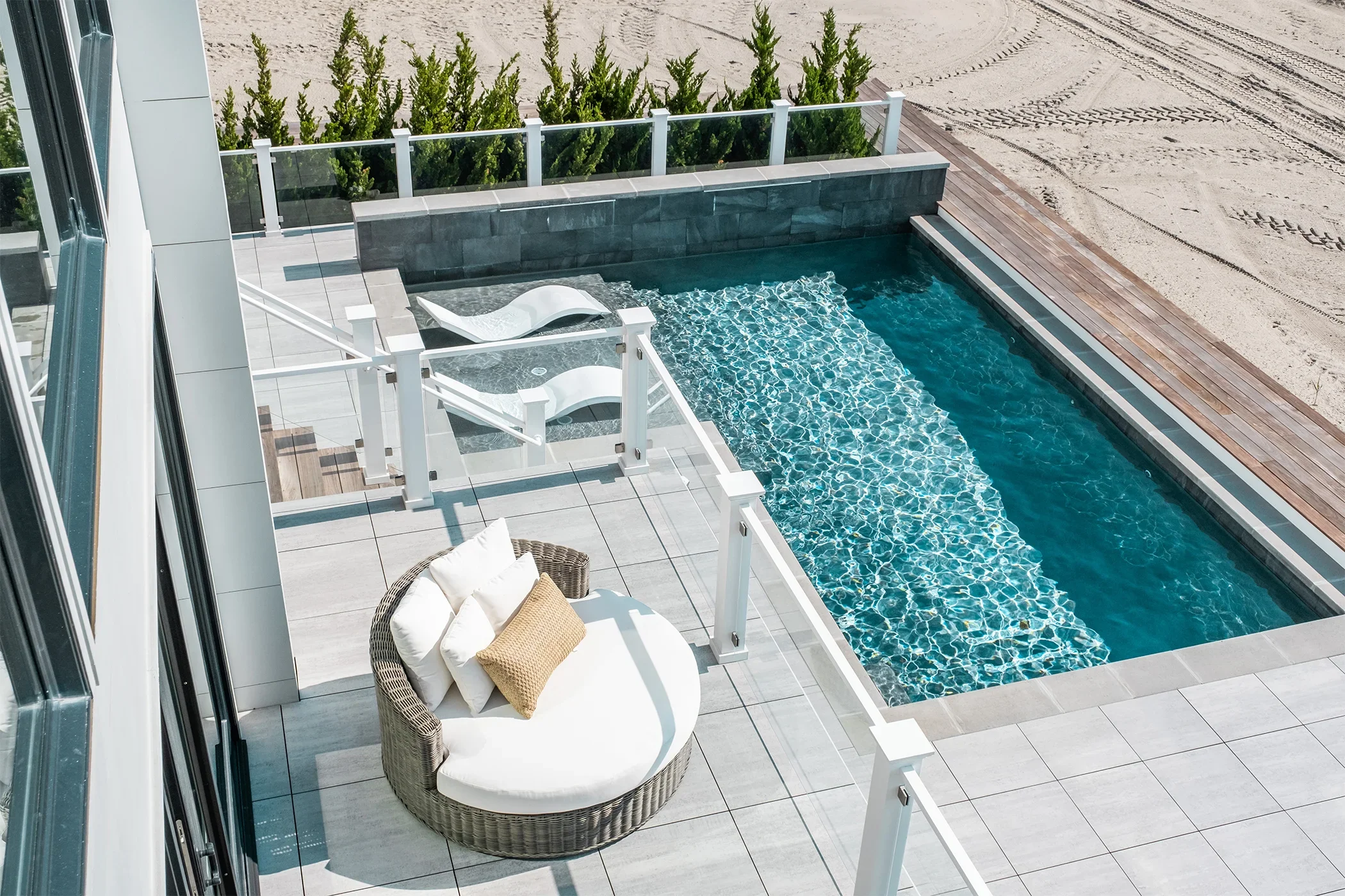 A modern outdoor balcony with a swimming pool, lounge chairs, and a cushioned outdoor seating area.