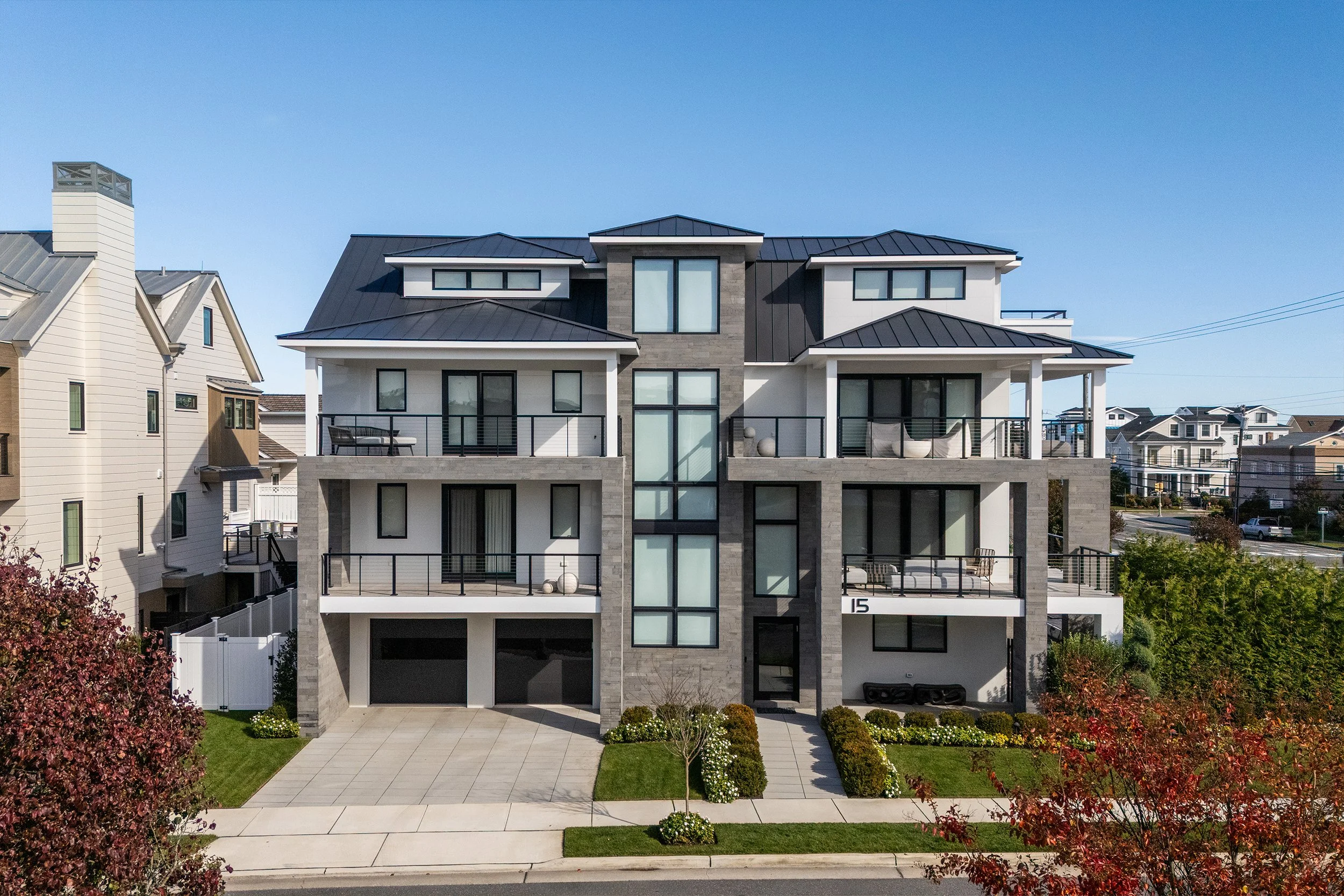 Modern multi-story residential building with balconies and large windows, surrounded by landscaped greenery and located in a suburban neighborhood.