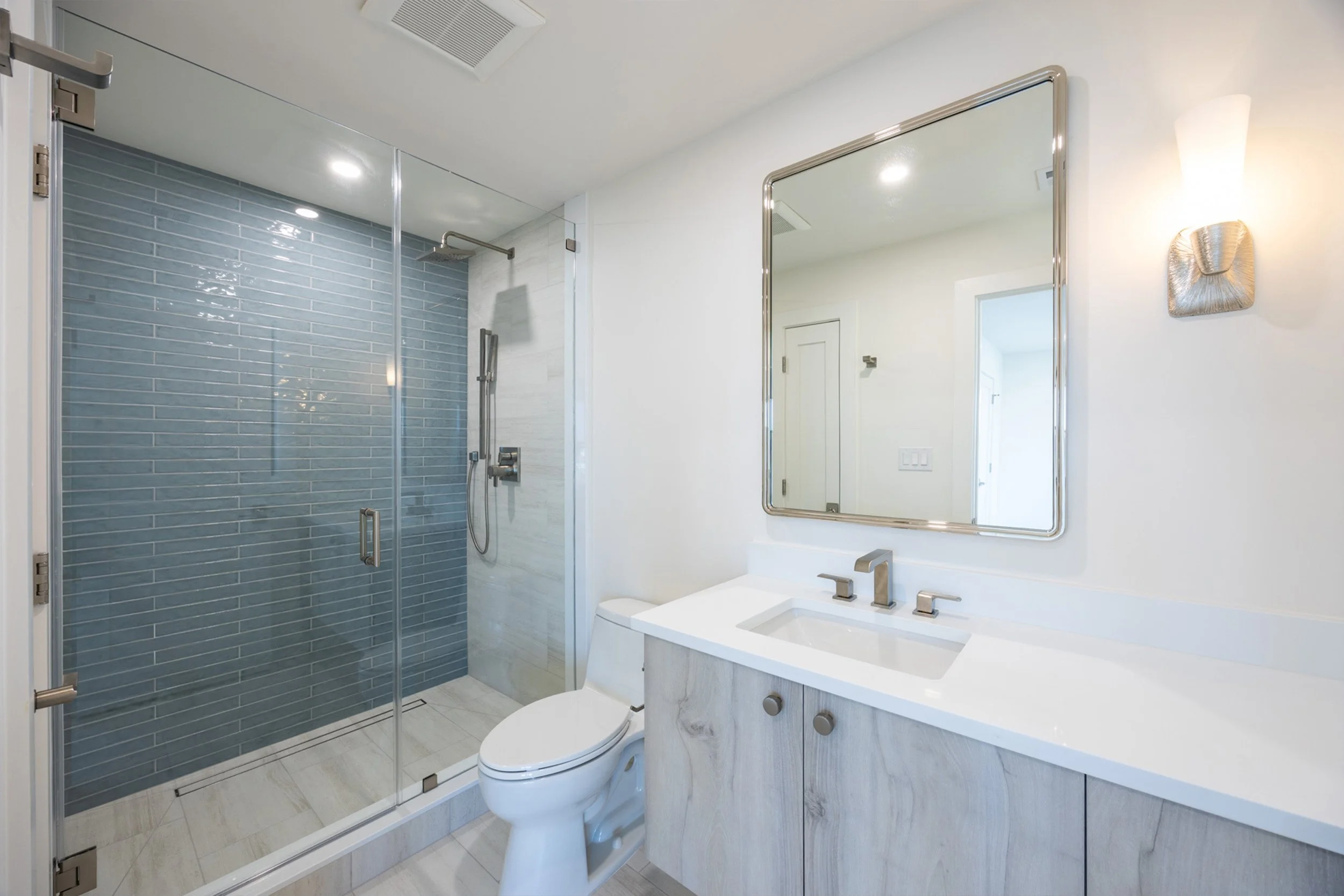 Modern bathroom with walk-in shower with glass doors, toilet, and white vanity with a mirror.