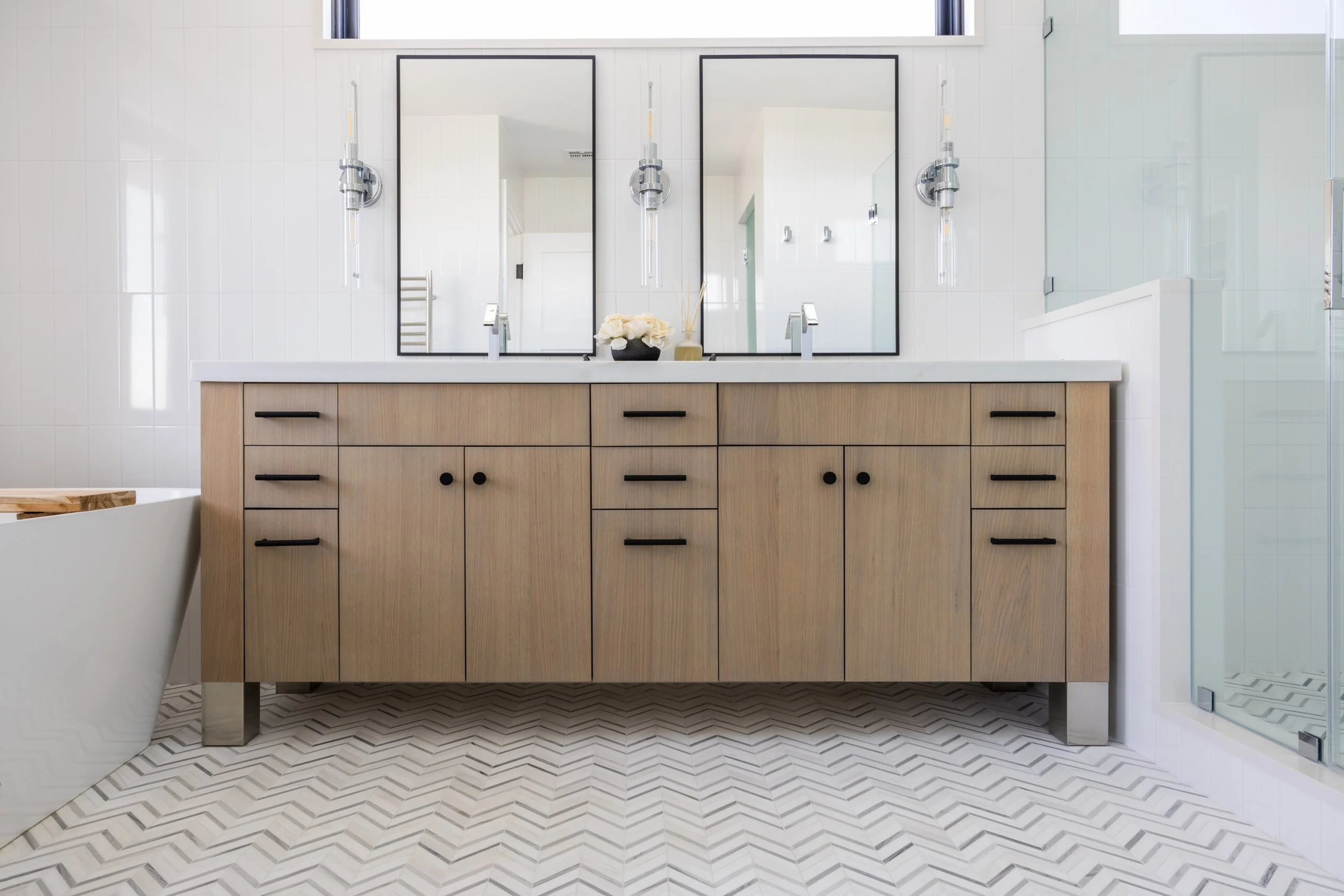 Modern bathroom with wooden vanity, two mirrors, black fixtures, white countertop, and a shower with glass door.