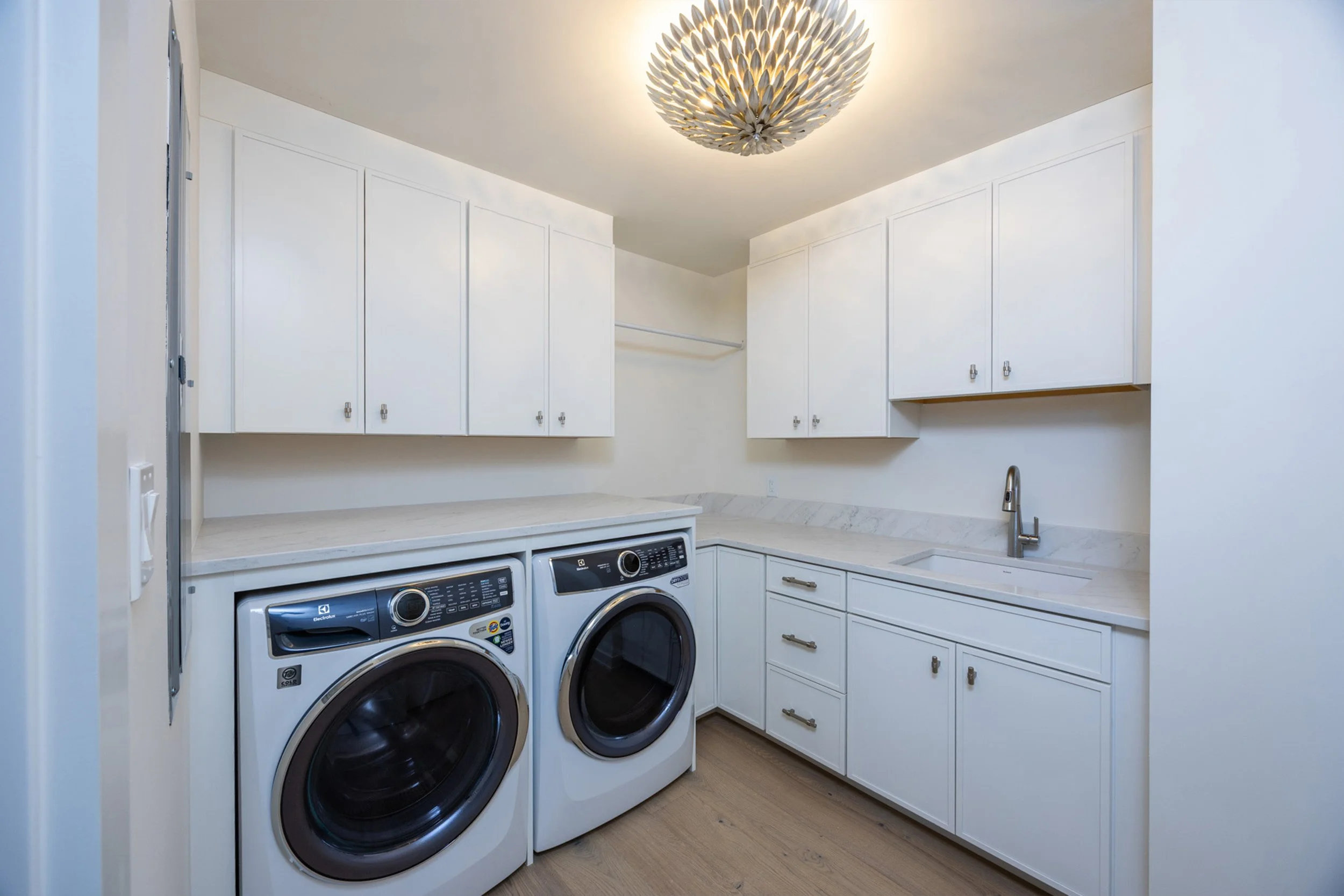 Laundry room with white cabinets, marble countertop, front-loading washing machine and dryer, small sink, and ceiling light fixture.