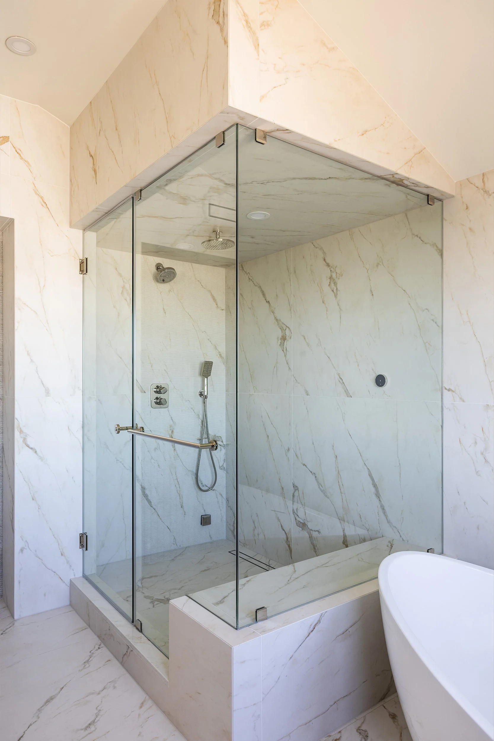 Bathroom shower with marble tiles, glass enclosure, and a handheld showerhead.