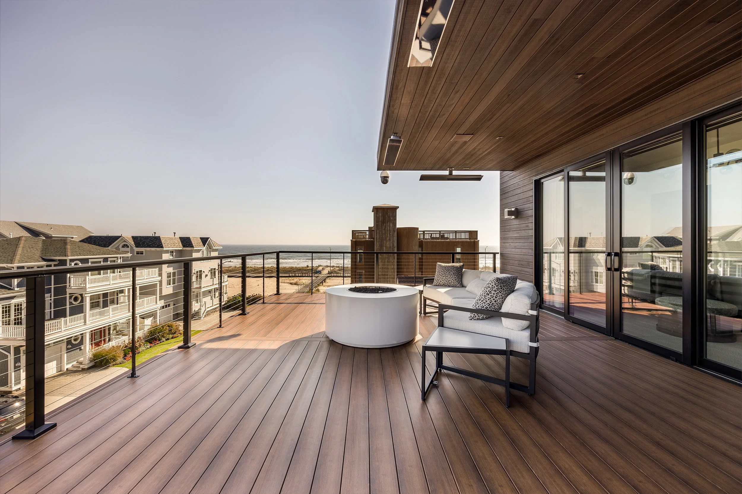 Modern balcony with wooden flooring, outdoor seating, and ocean view, sliding glass doors leading inside.