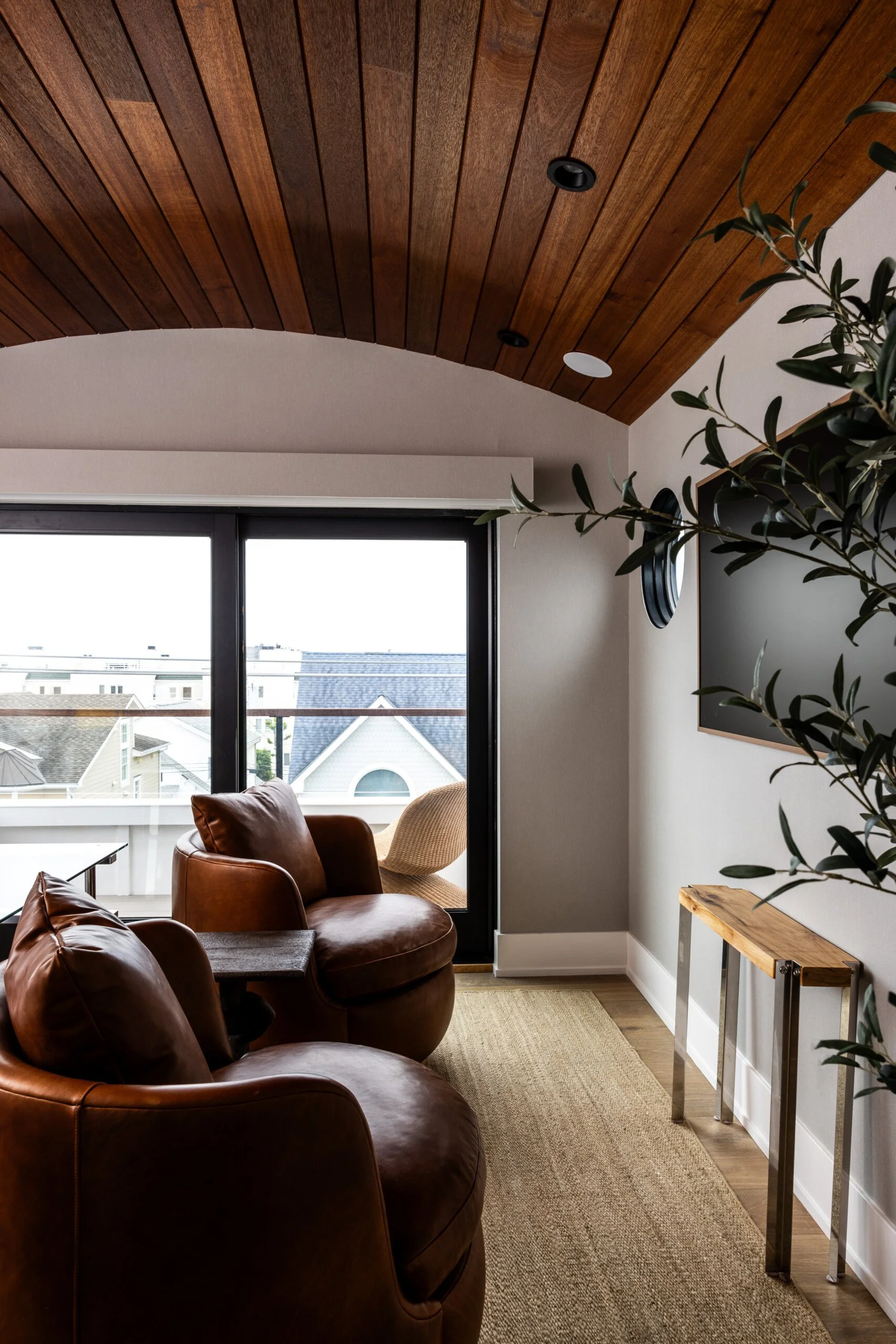 Cozy living room with leather armchairs, a sliding glass door leading to a balcony, and a wooden ceiling.