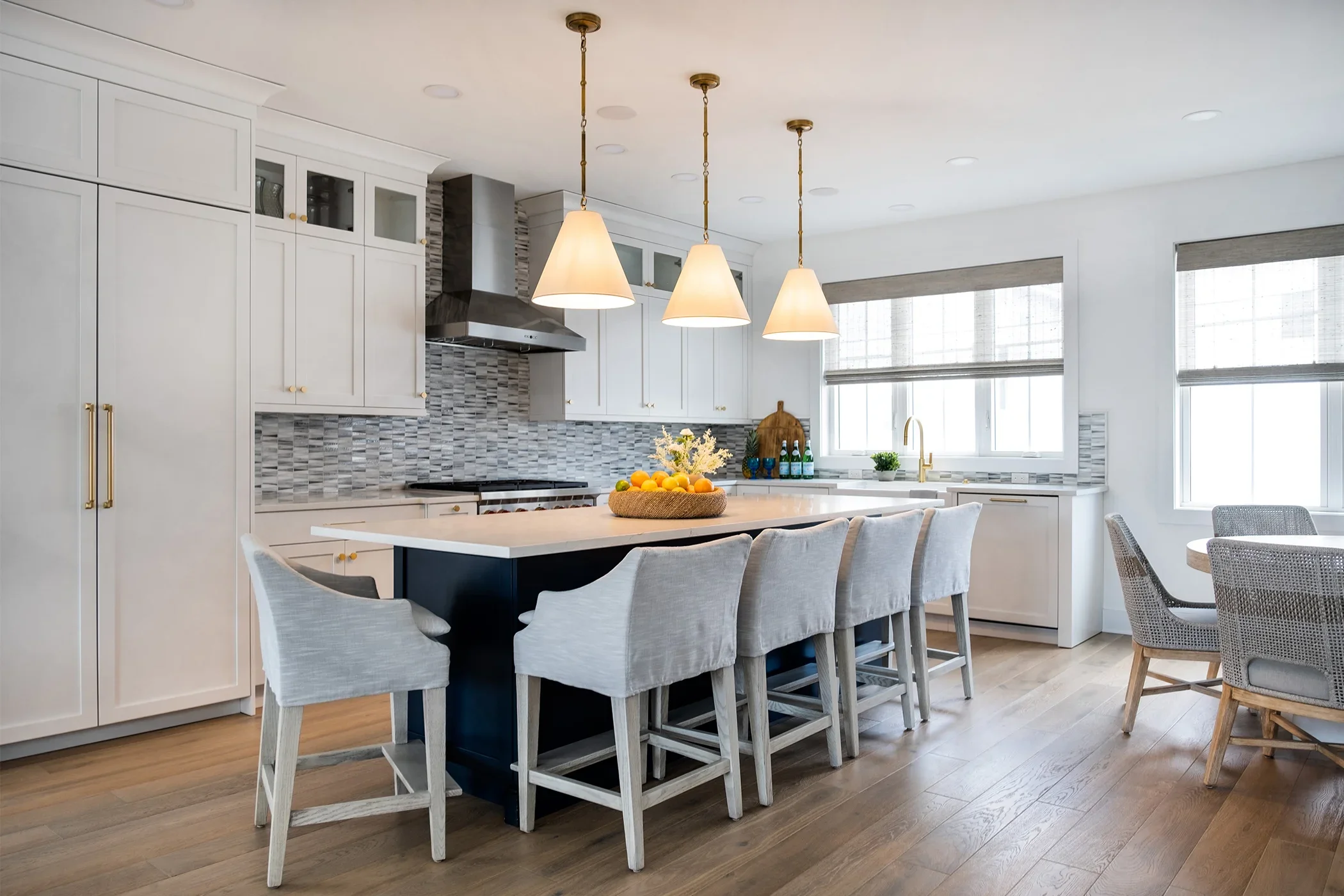 Modern kitchen with white cabinets, gray backsplash, island with seating, three pendant lights, large windows, and wooden flooring.