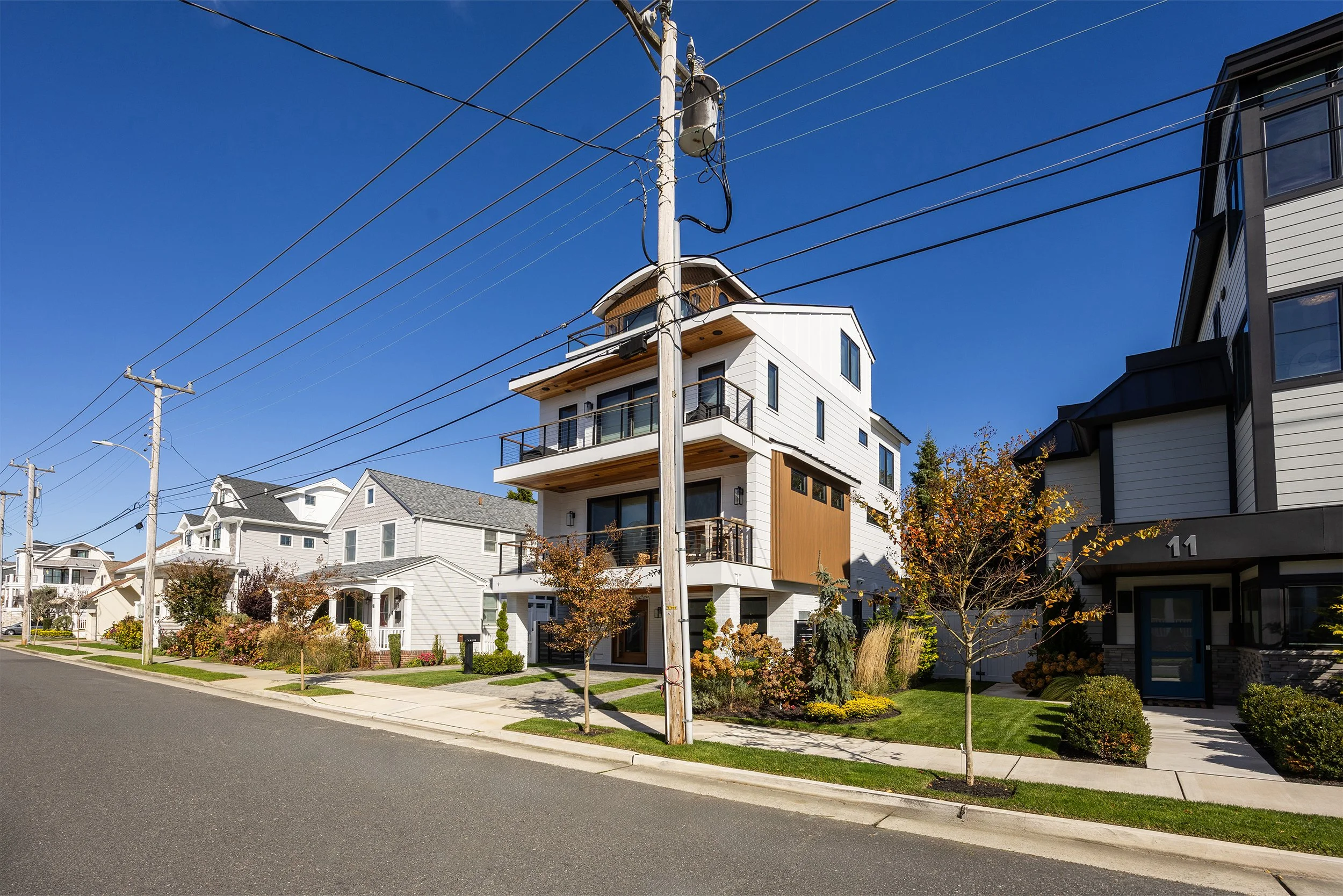 Modern multi-story residential buildings with landscaped front yards, trees, and a clear blue sky.