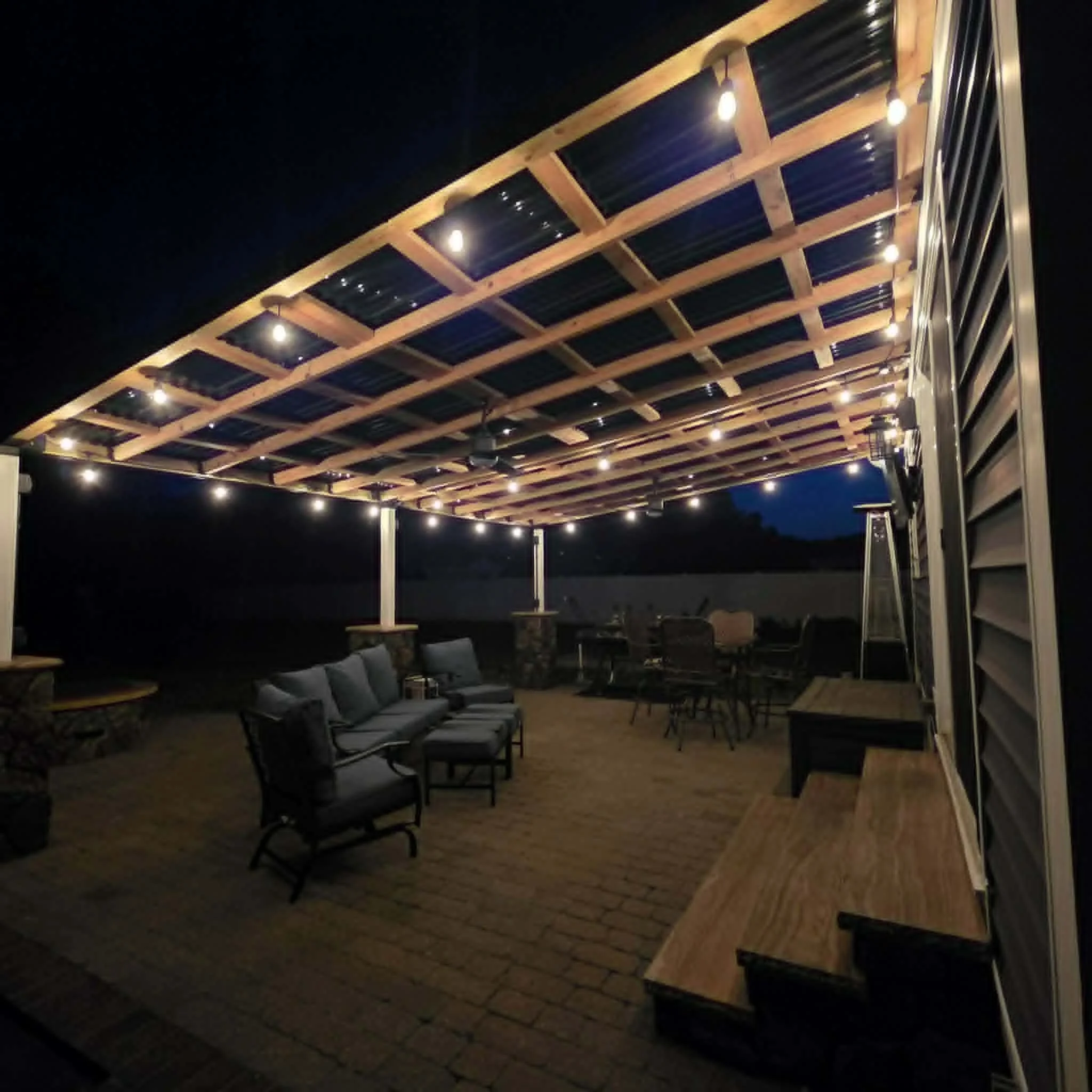 Nighttime outdoor patio area with string lights, wooden beams, and cushioned seating.