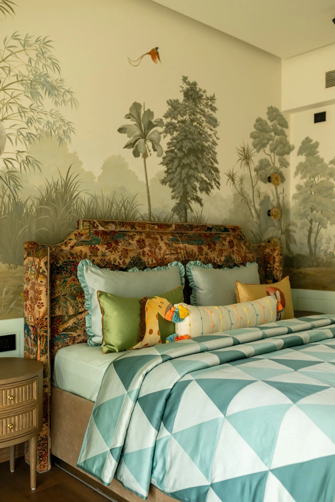 Interior of a bedroom with botanical wallpaper featuring trees and plants, and a bed with striped bedding and colorful pillows.