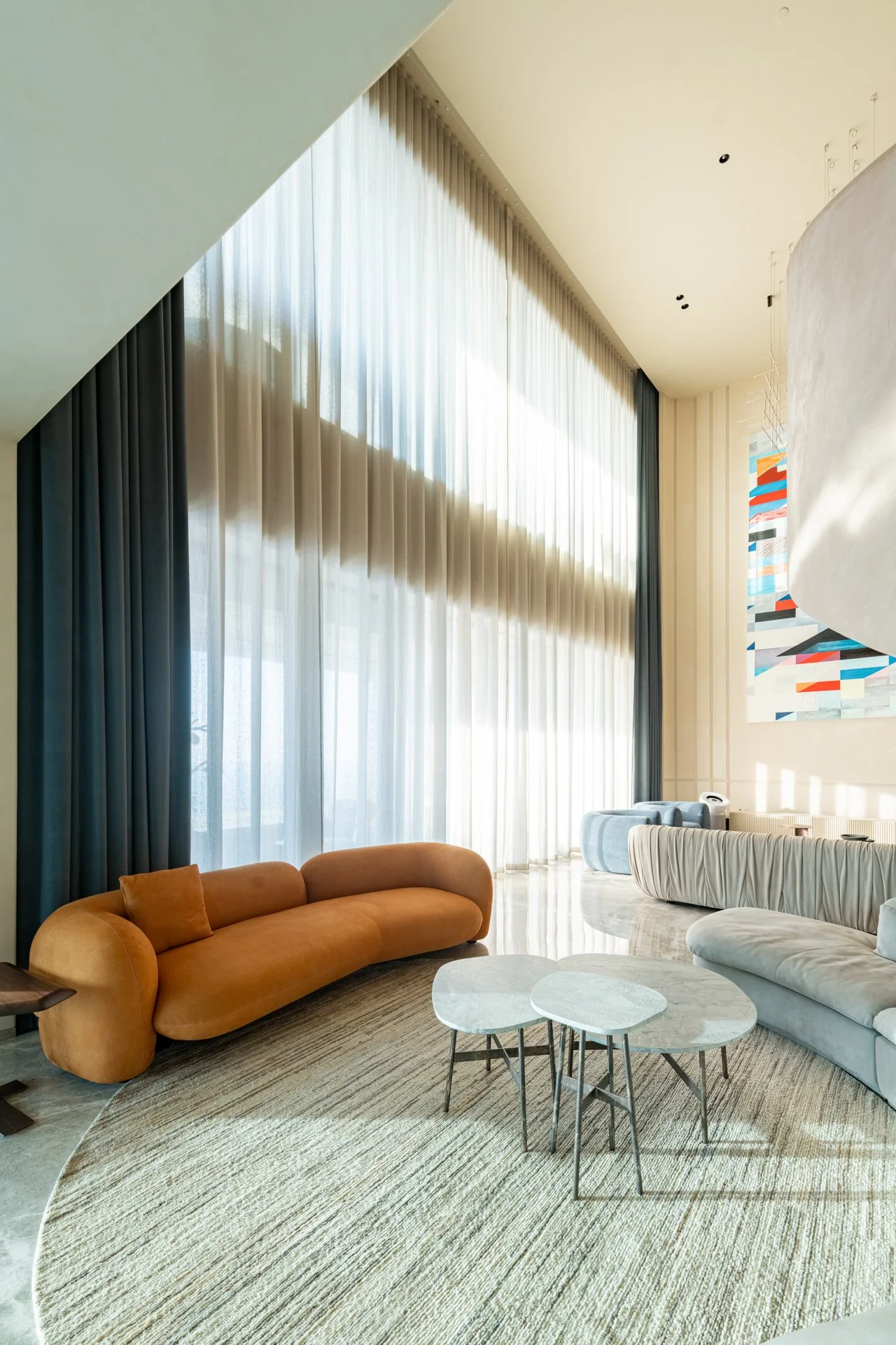Modern hotel lobby with large floor-to-ceiling curtains, contemporary sofas, a round area rug, and abstract wall art.
