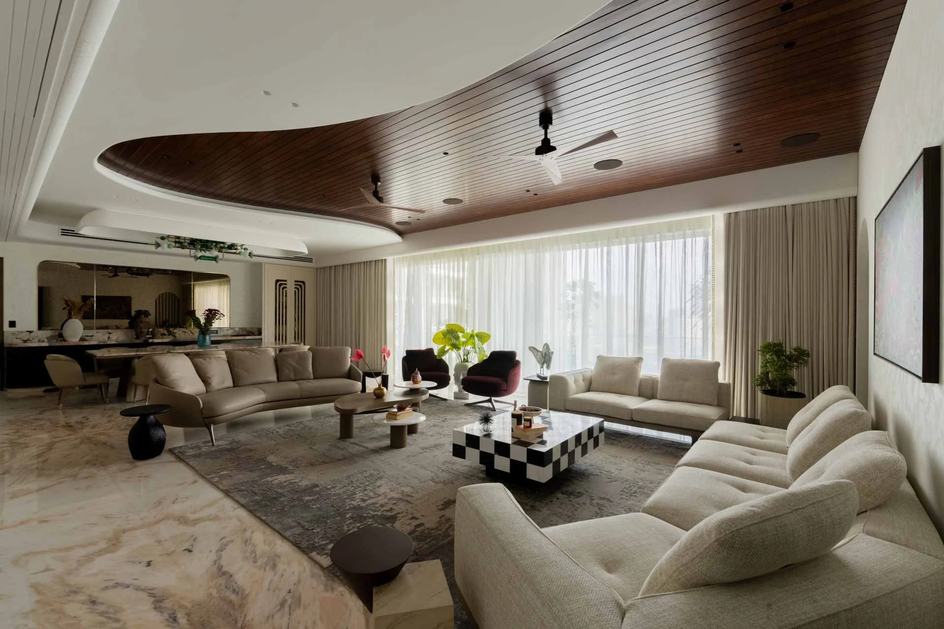 Modern living room with beige sofas, a marble coffee table, and large windows with curtains, decorated with plants and artwork on the wall.