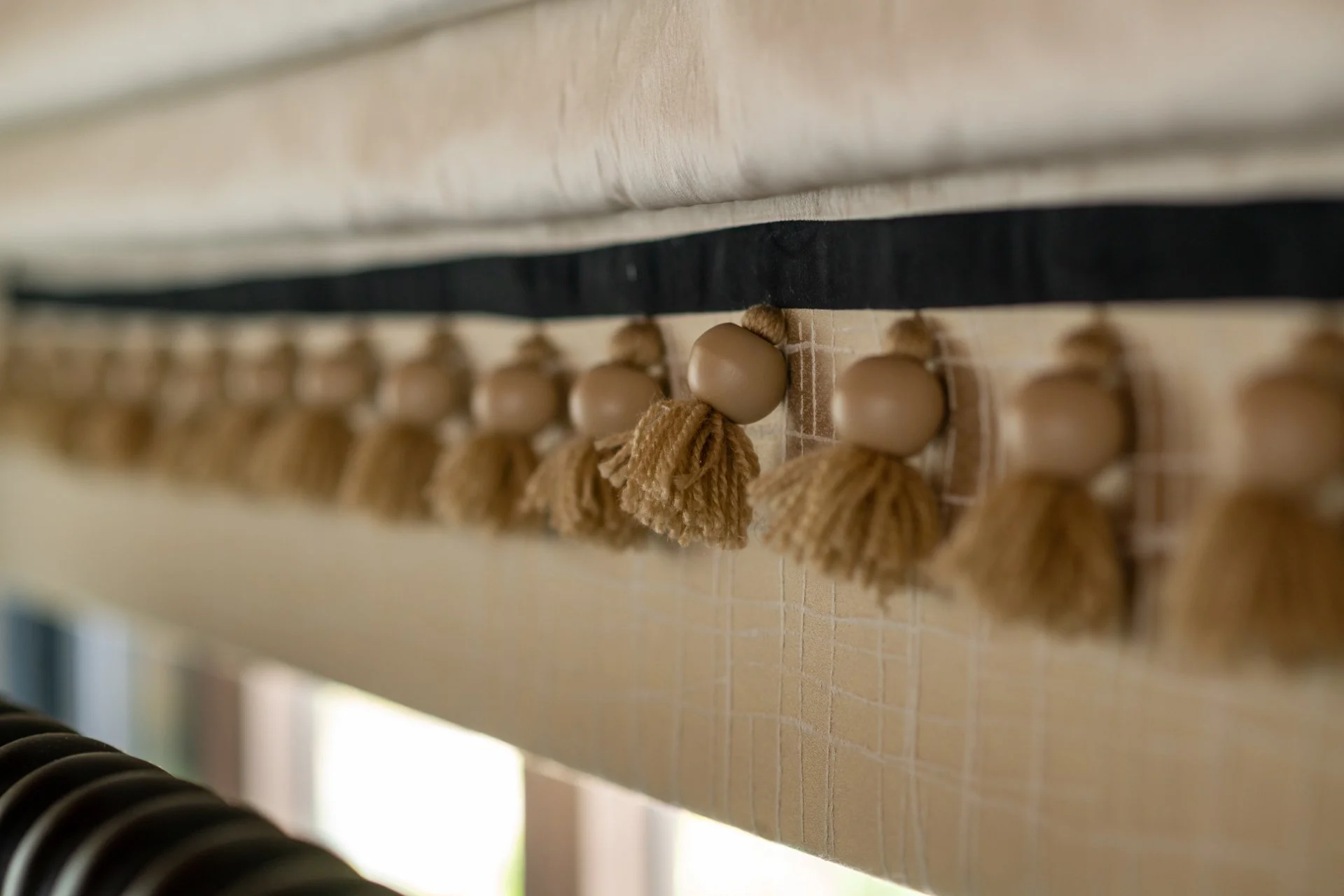 Close-up of decorative tassels hanging from a black ribbon, attached to a wooden surface with a light-colored background.