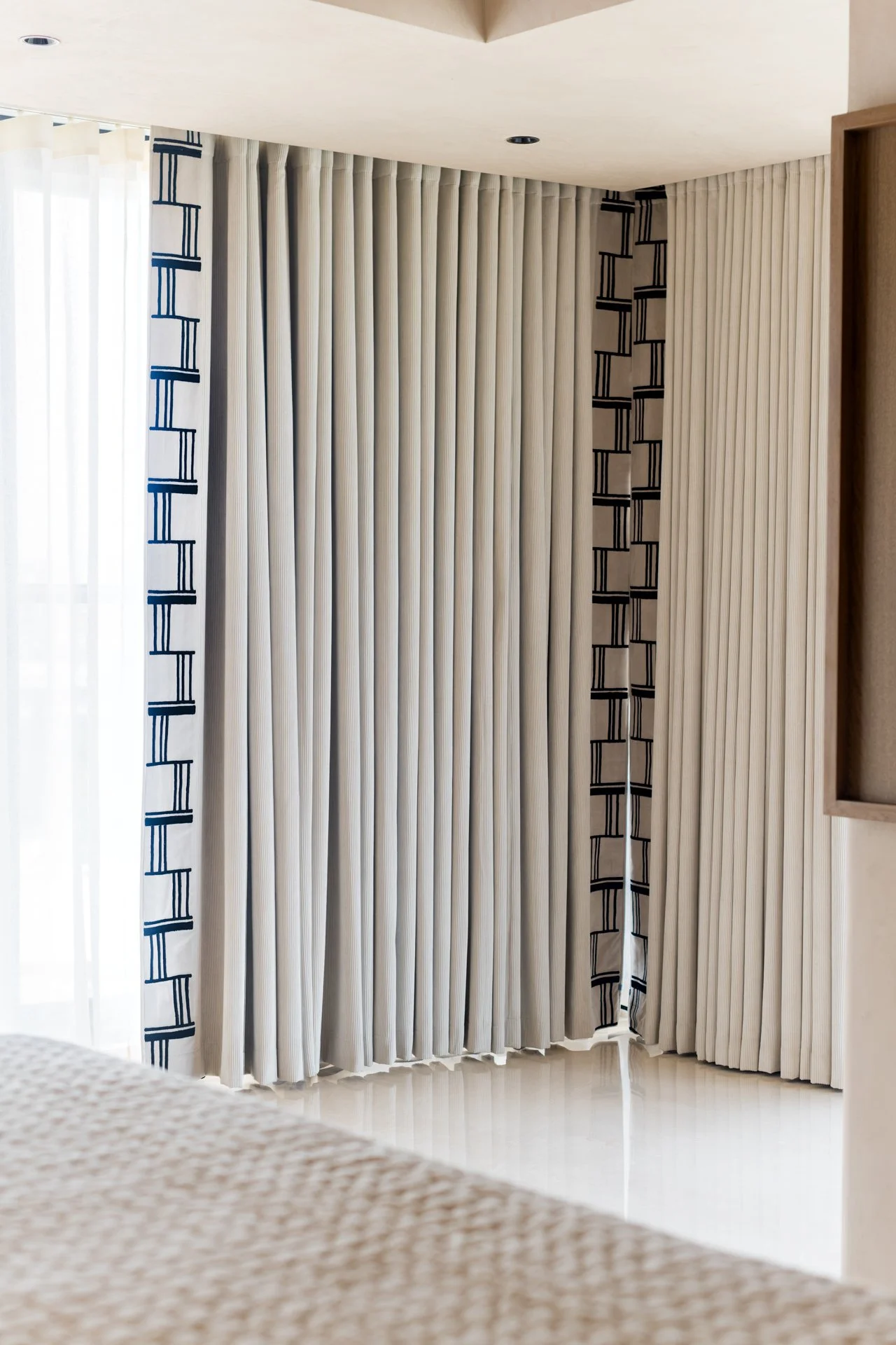 Cream-colored curtains with blue and black geometric patterns hanging in a room with cream walls and a beige ceiling.