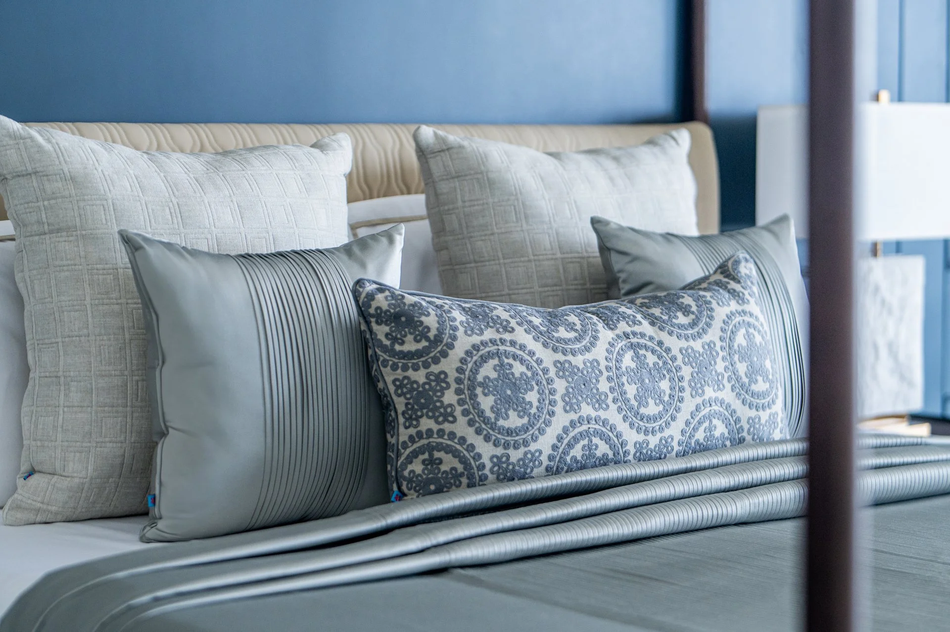 Close-up of a neatly made bed with silk and patterned decorative pillows, in a room with blue walls and bedside lamps.