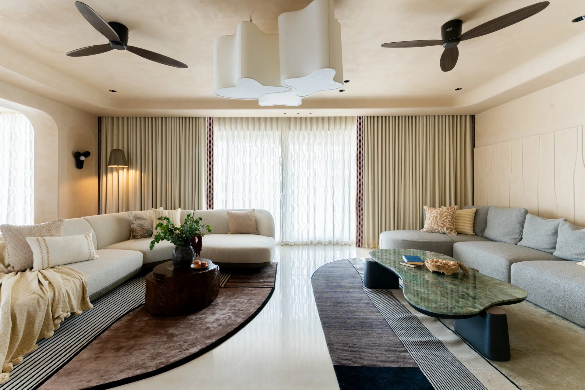 Living room with cream-colored curved sofa, beige curtains, and modern ceiling fans and light fixtures.