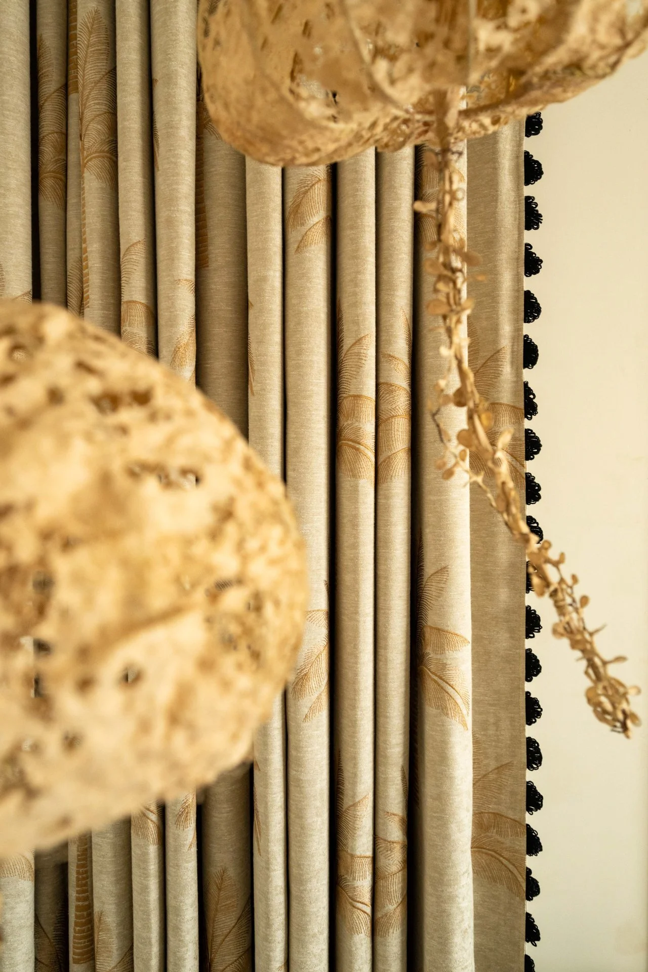 Close-up view of beige curtains with a leaf pattern and black trim, with a textured brown decorative object in the foreground.