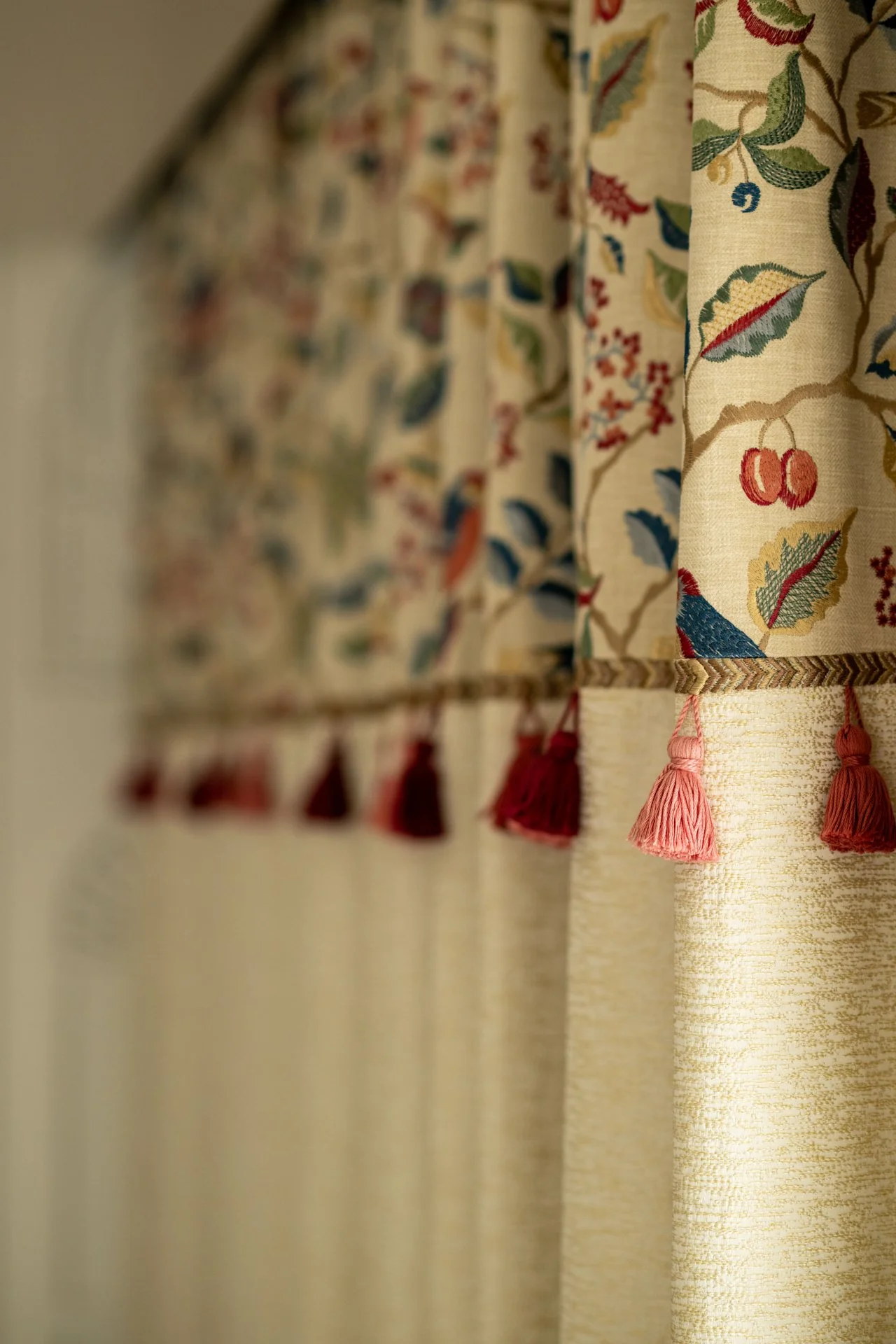Close-up view of floral patterned curtains with pink tassels hanging at the bottom, seen from a side angle.