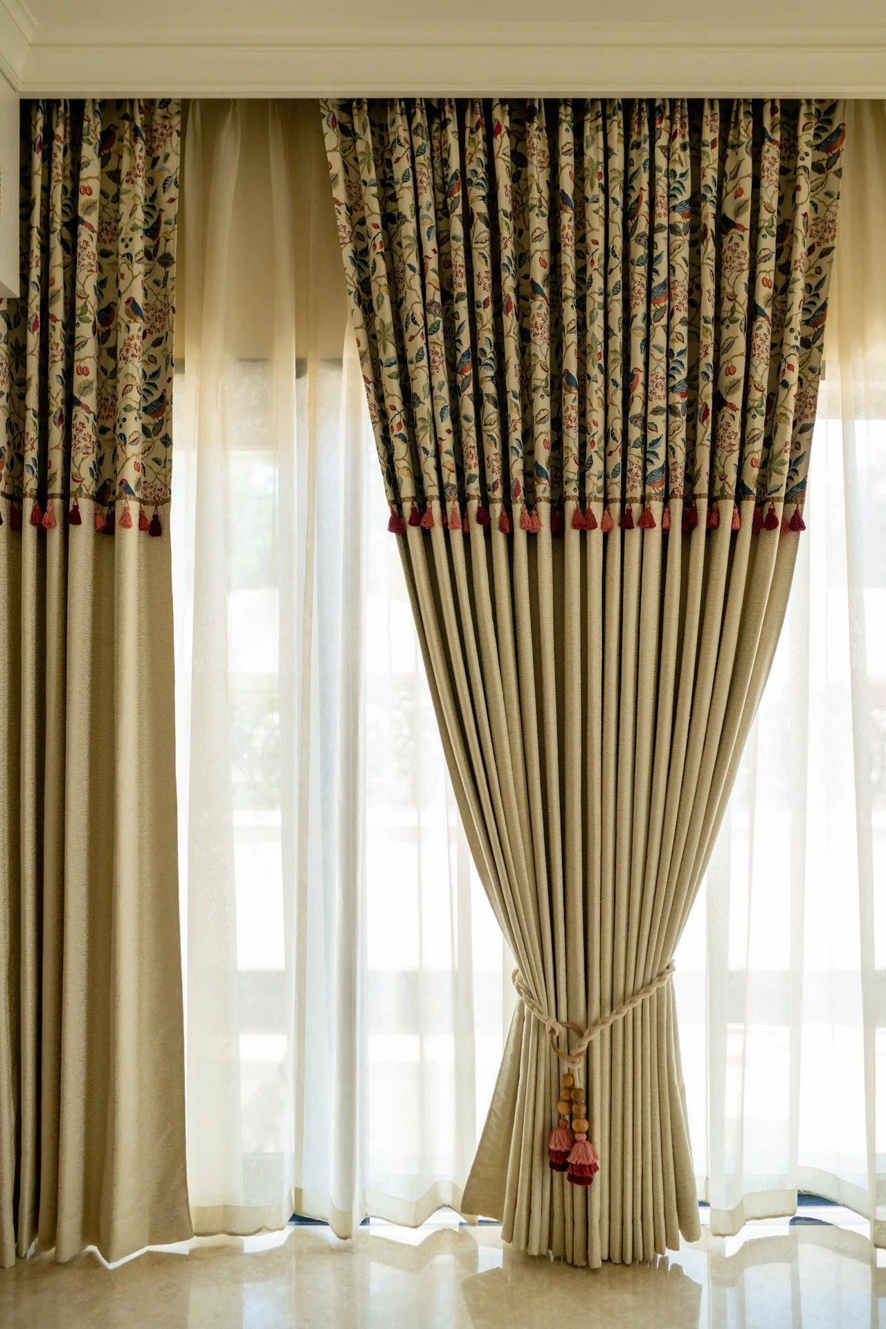 Elegant window curtains with floral and bird pattern, tied back with a tassel.
