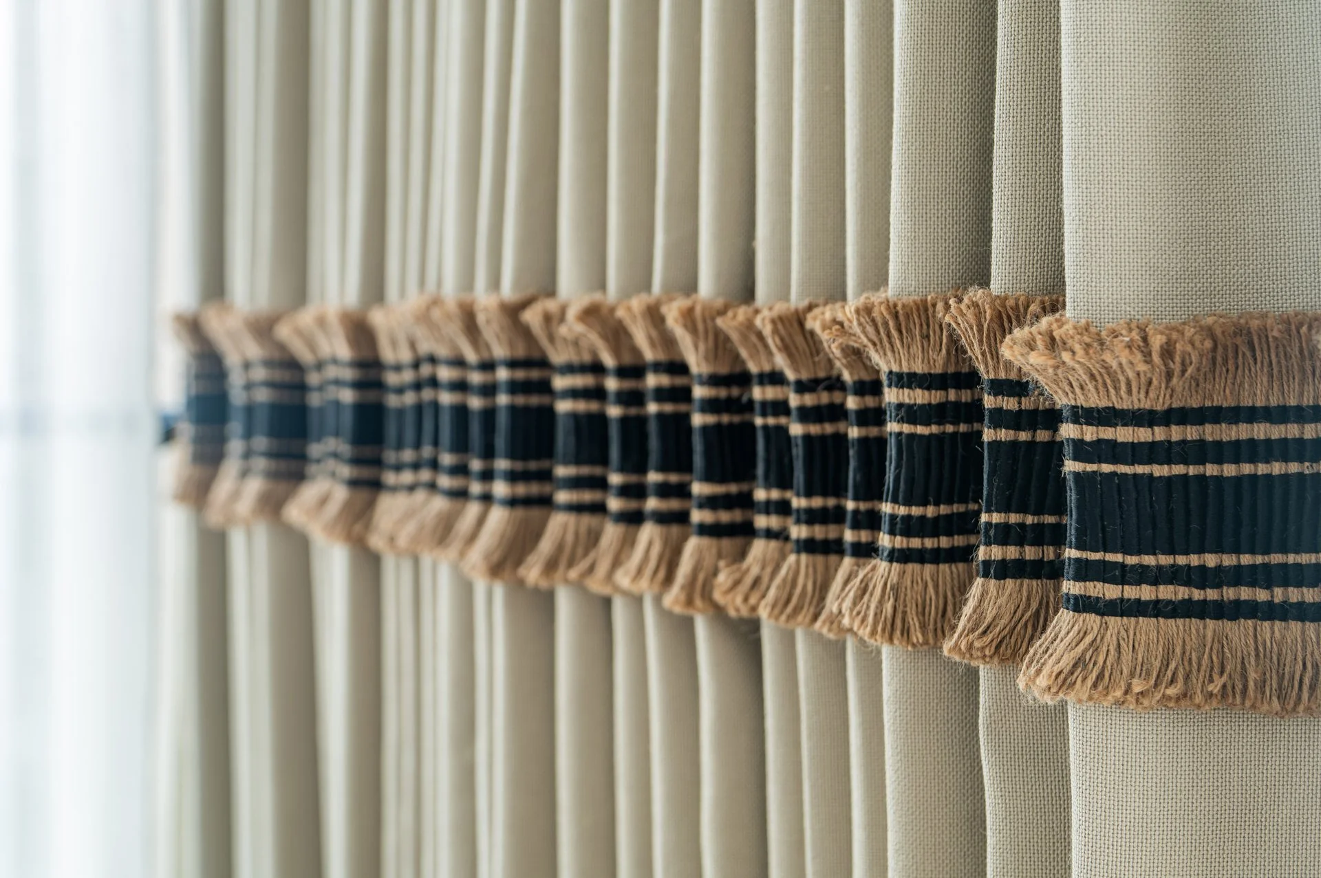 A row of window blinds with pulled-down fabric valances that have a striped pattern and fringed edges.
