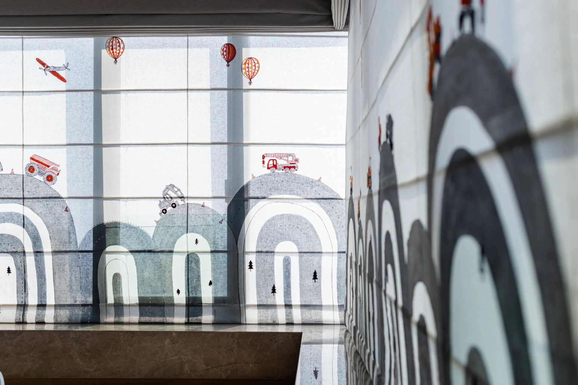 Decorative mural featuring mountain, construction truck, trees, and hot air balloons seen through a window with horizontal blinds.